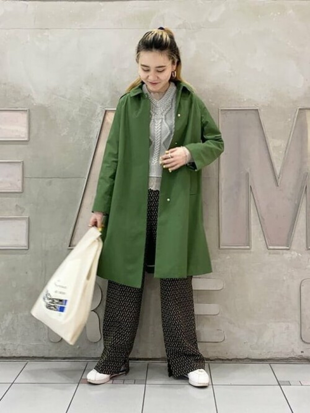 グリーン系のステンカラーコート、イエロー系のその他パンツ、ホワイト系のエコバッグ/サブバッグを着用したレディースの春コーディネートの1枚目の写真