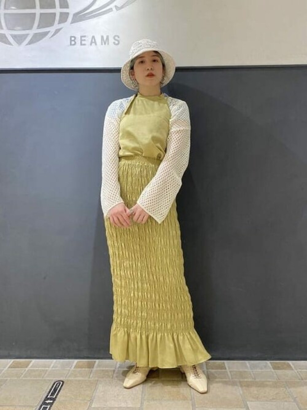 イエロー系のスカート、イエロー系のシャツ/ブラウス、ベージュ系のニット/セーターを着用したレディースの春コーディネートの1枚目の写真