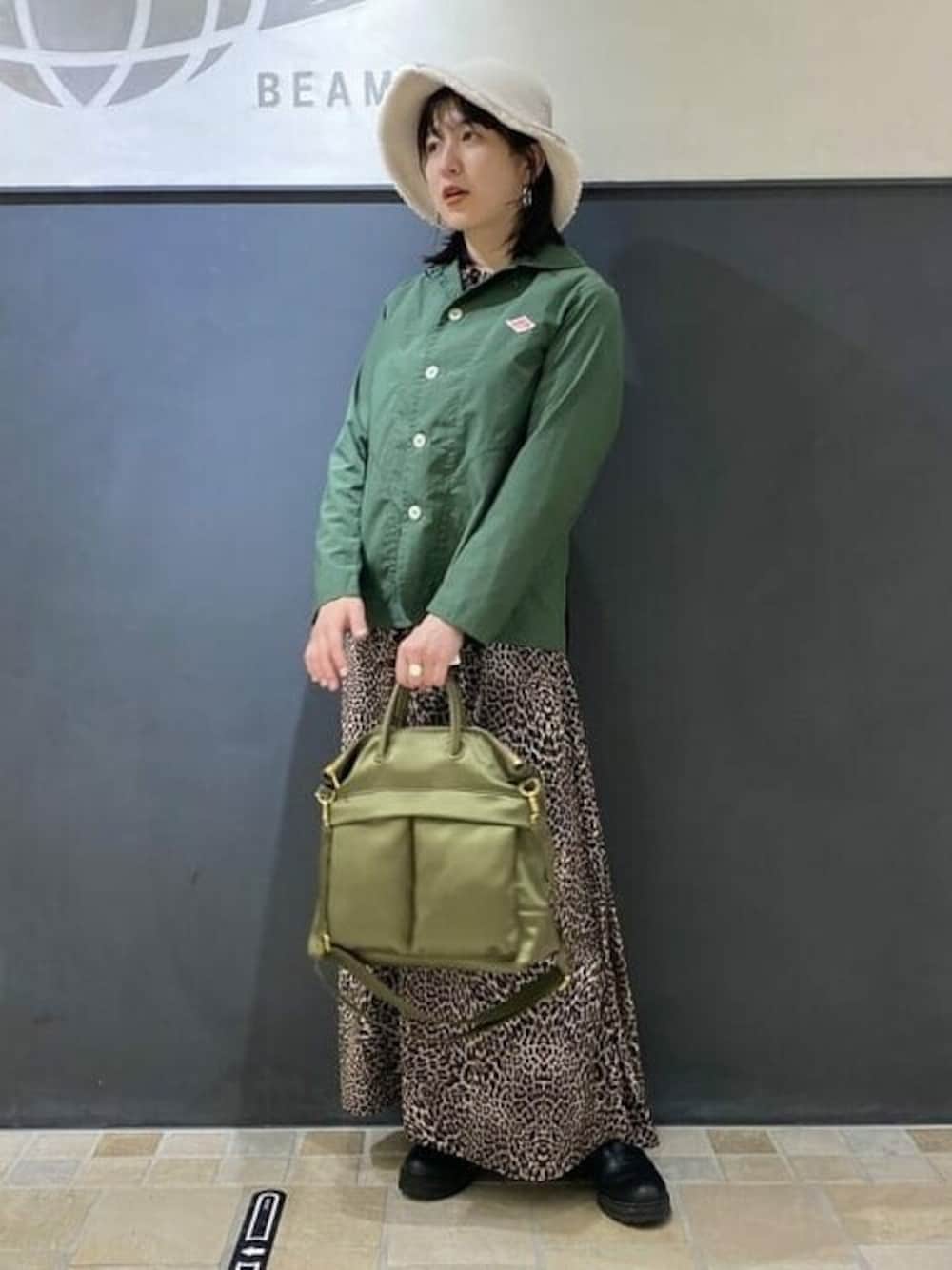 グリーン系のトートバッグ、グリーン系のカバーオール、ベージュ系のハットを着用したレディースの秋コーディネートの1枚目の写真