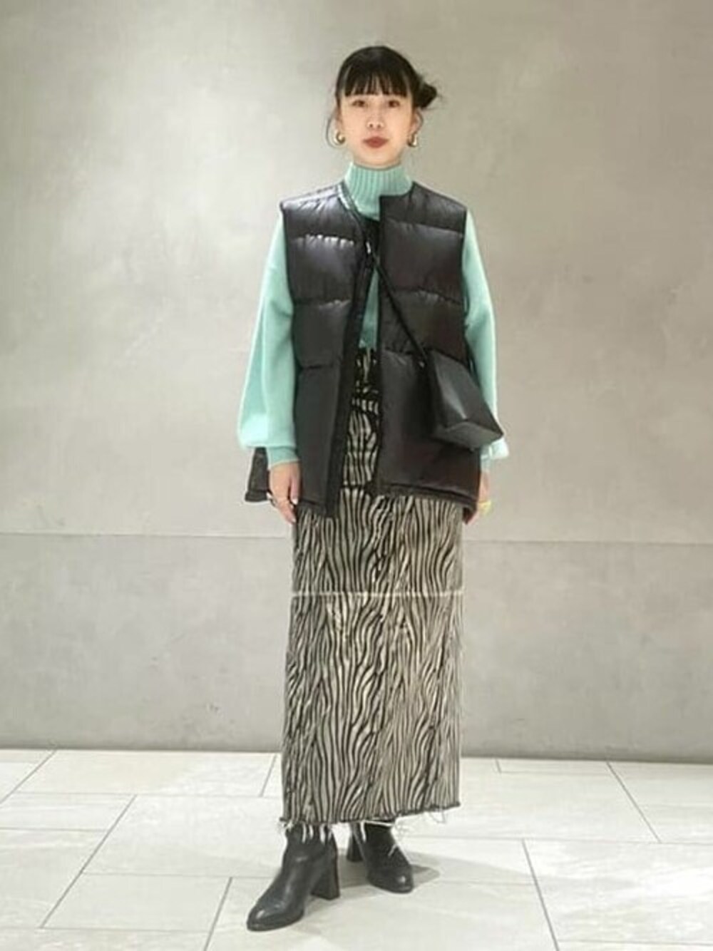 グリーン系のニット/セーター、ブラック系のベスト、ブラック系のブーツを着用したレディースの秋コーディネートの1枚目の写真