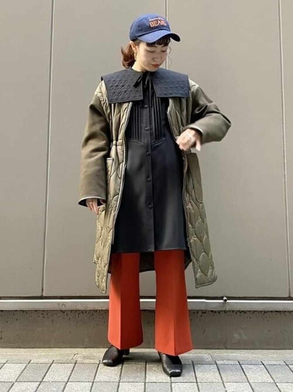 グリーン系のノーカラーコート、ブラック系のワンピース、オレンジ系のその他パンツを着用したレディースの秋コーディネートの1枚目の写真