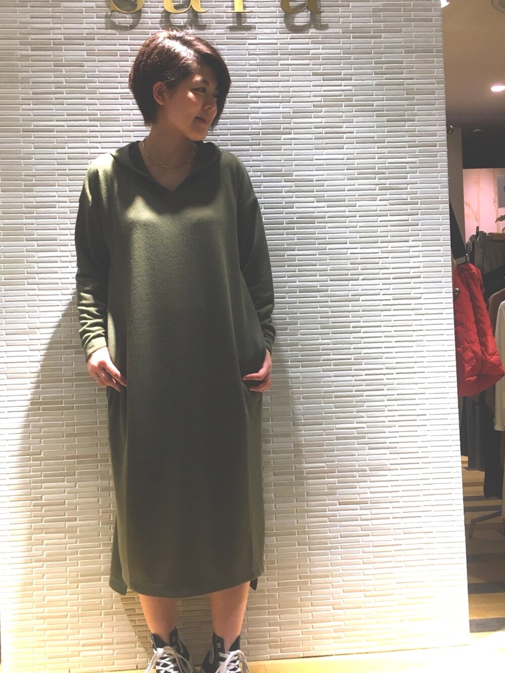 グリーン系のワンピース、ブラック系のスニーカー、ゴールド系のチョーカーを着用したレディースの秋コーディネートの1枚目の写真