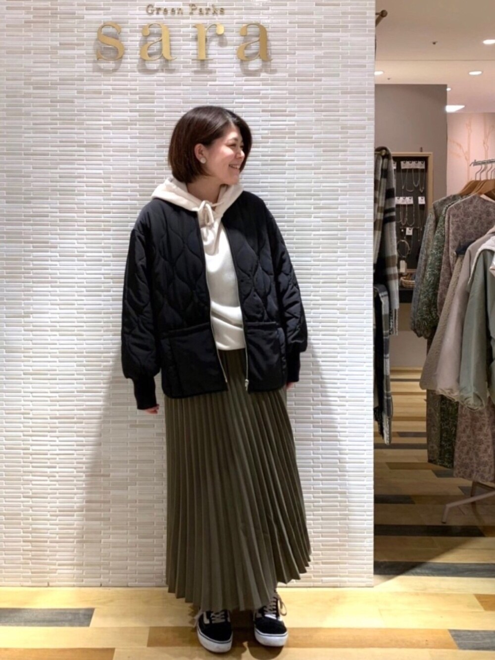 ホワイト系のパーカー、グリーン系のスカート、ブラック系のその他アウターを着用したレディースの冬コーディネートの1枚目の写真