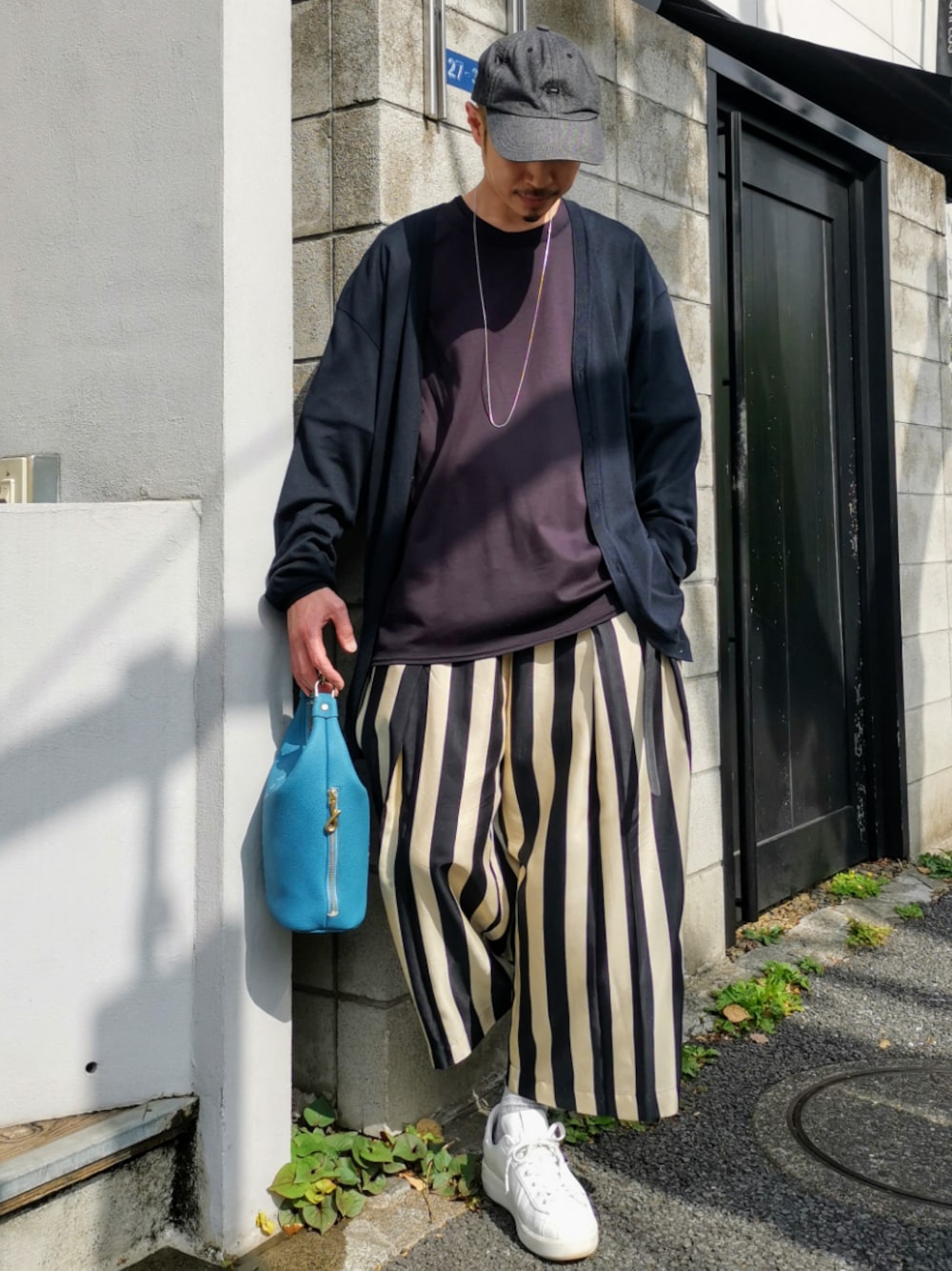 ホワイト系のスニーカー、ブルー系のハンドバッグ、ブルー系のトップスを着用したメンズの春コーディネートの1枚目の写真