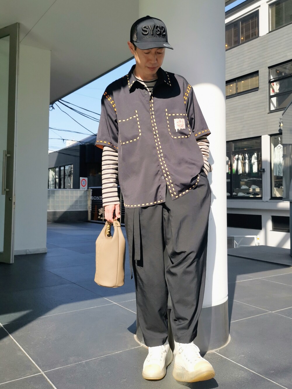 グレー系のハンドバッグ、ホワイト系のスニーカー、グレー系のTシャツ/カットソーを着用したメンズの春コーディネートの1枚目の写真