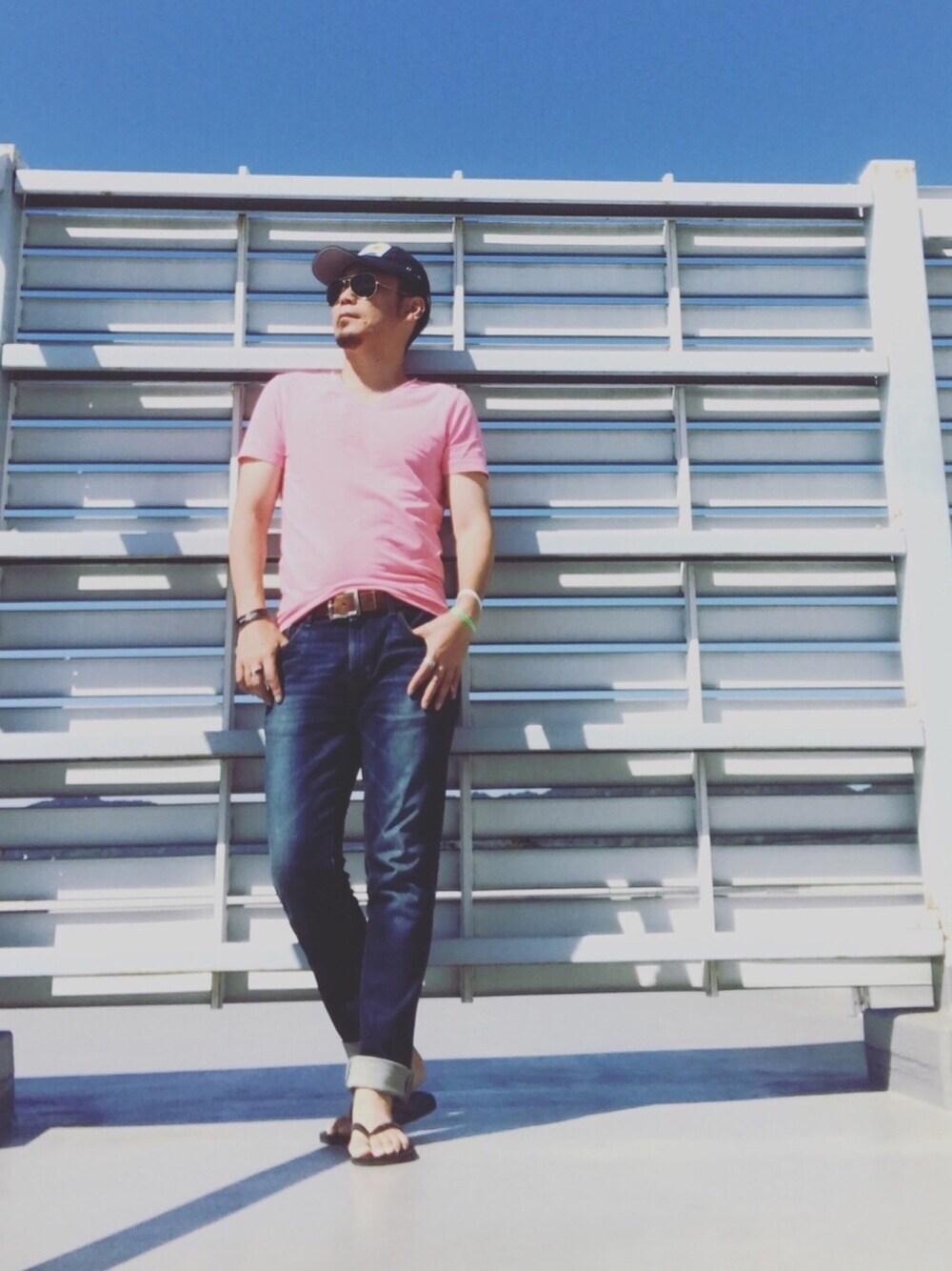 ブルー系のデニムパンツ、ブラック系のサンダル、ピンク系のTシャツ/カットソーを着用したメンズの夏コーディネートの1枚目の写真