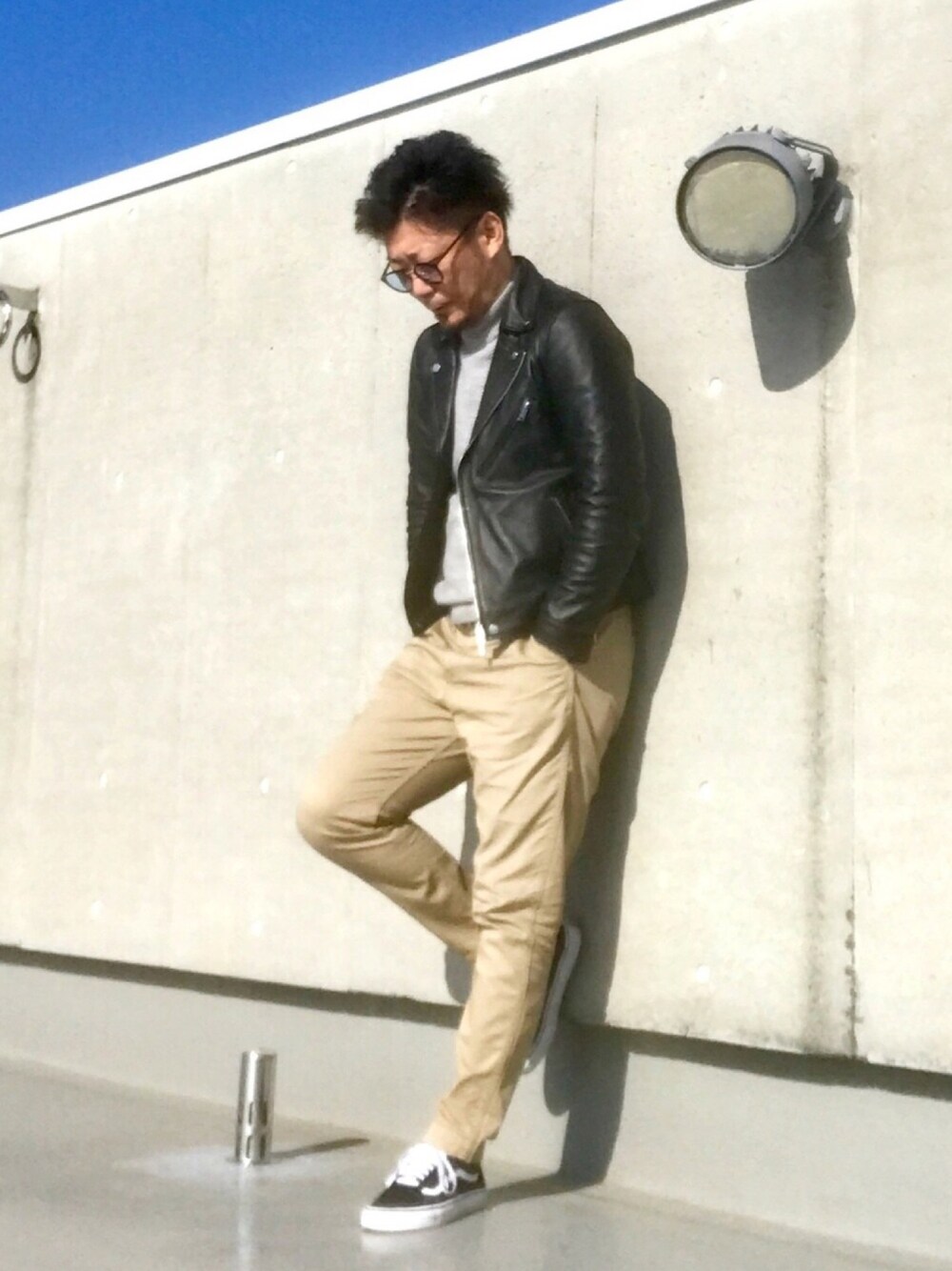 ブラック系のライダースジャケット、ブラック系のスニーカー、ベージュ系のチノパンツを着用したメンズの春コーディネートの1枚目の写真