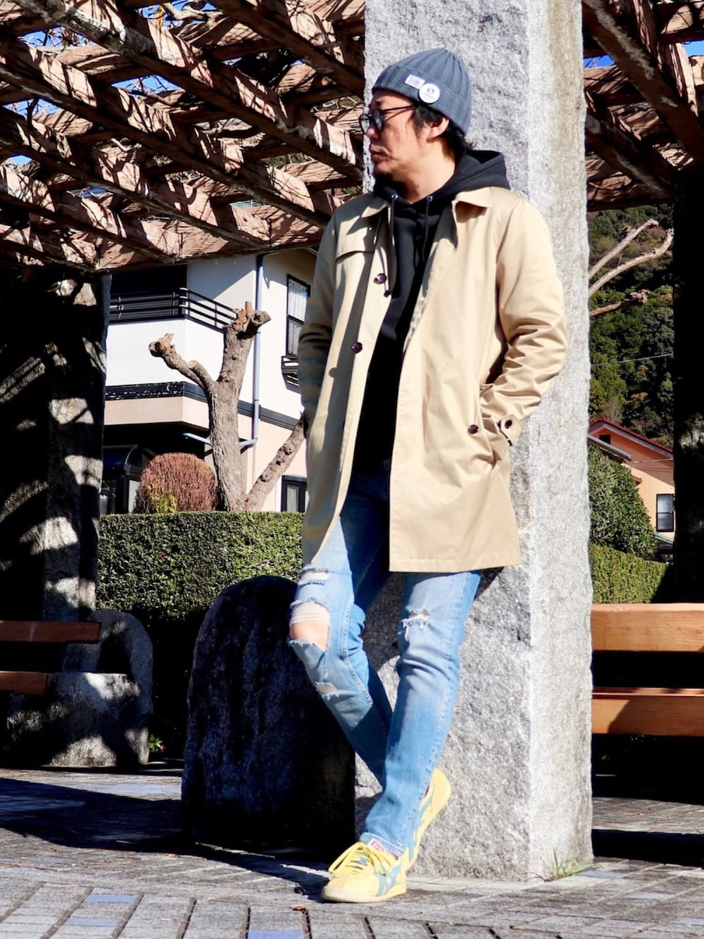 ブラック系のパーカー、ブルー系のデニムパンツ、ベージュ系のステンカラーコートを着用したメンズの冬コーディネートの1枚目の写真