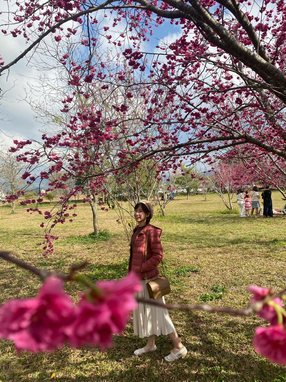 レッド系のダウンジャケット/コート、ベージュ系のハンドバッグ、ホワイト系のスリッポンを着用したレディースの冬コーディネートの1枚目の写真