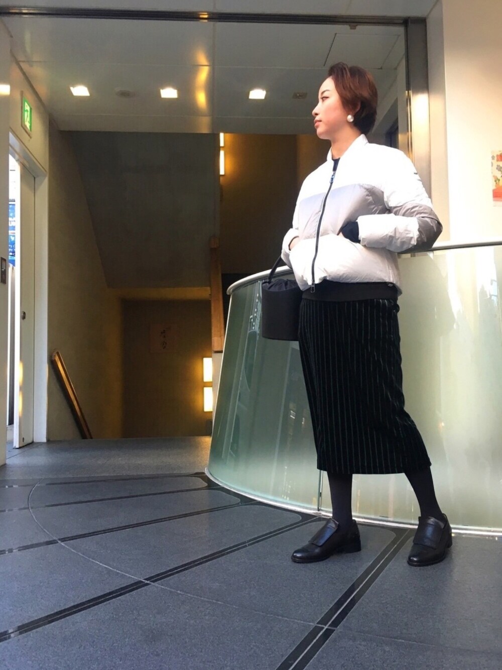 ブラック系のショルダーバッグ、ブラック系のスカート、ブラック系のローファーを着用したレディースの冬コーディネートの1枚目の写真