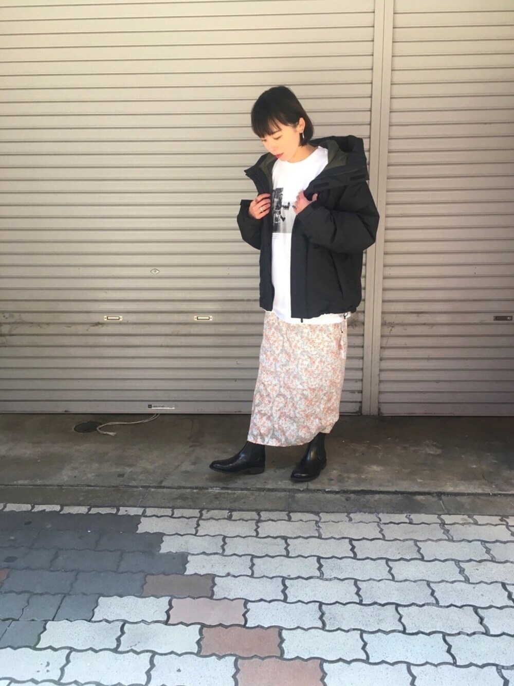 ブルー系のスカート、ブラック系のドレスシューズ、ブラック系のダウンジャケット/コートを着用したレディースの冬コーディネートの1枚目の写真