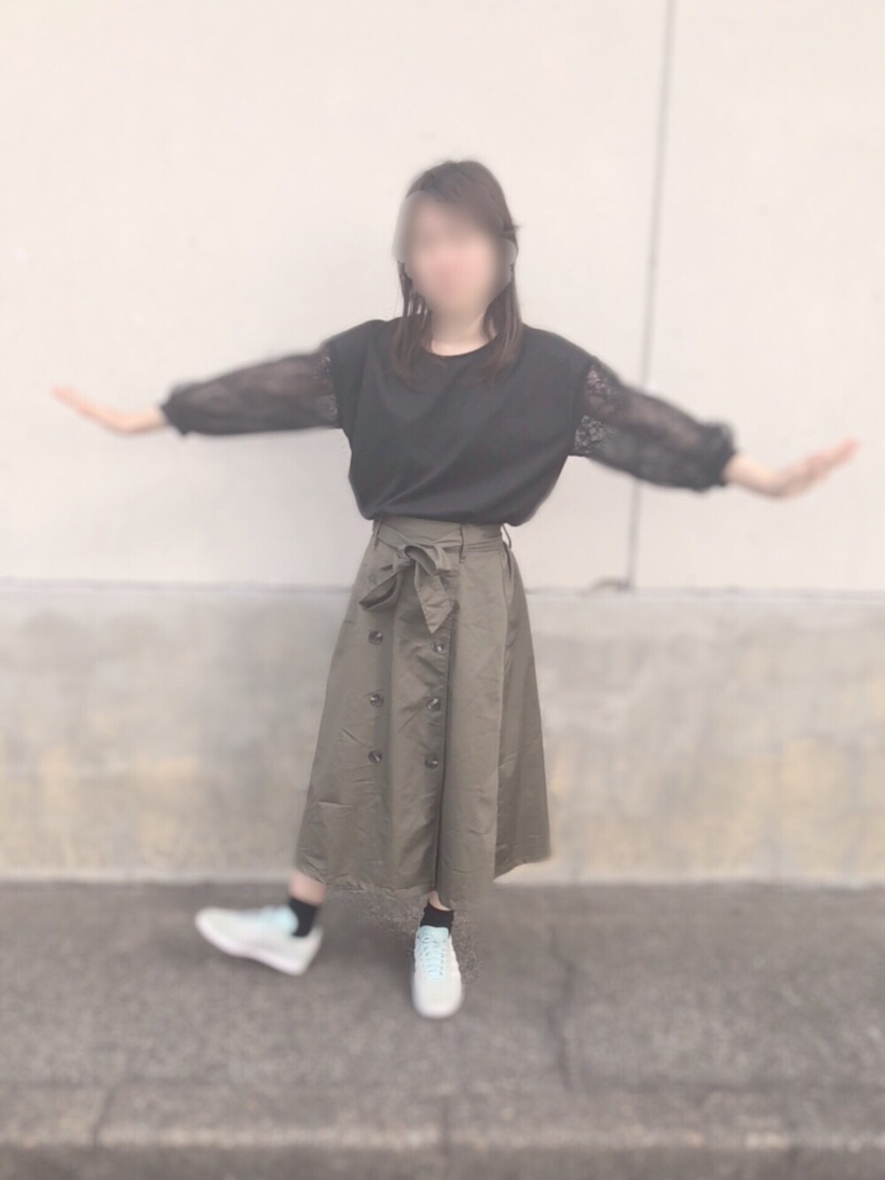 グリーン系のスカート、ブラック系のトップス、ブルー系のスニーカーを着用したレディースの秋コーディネートの1枚目の写真