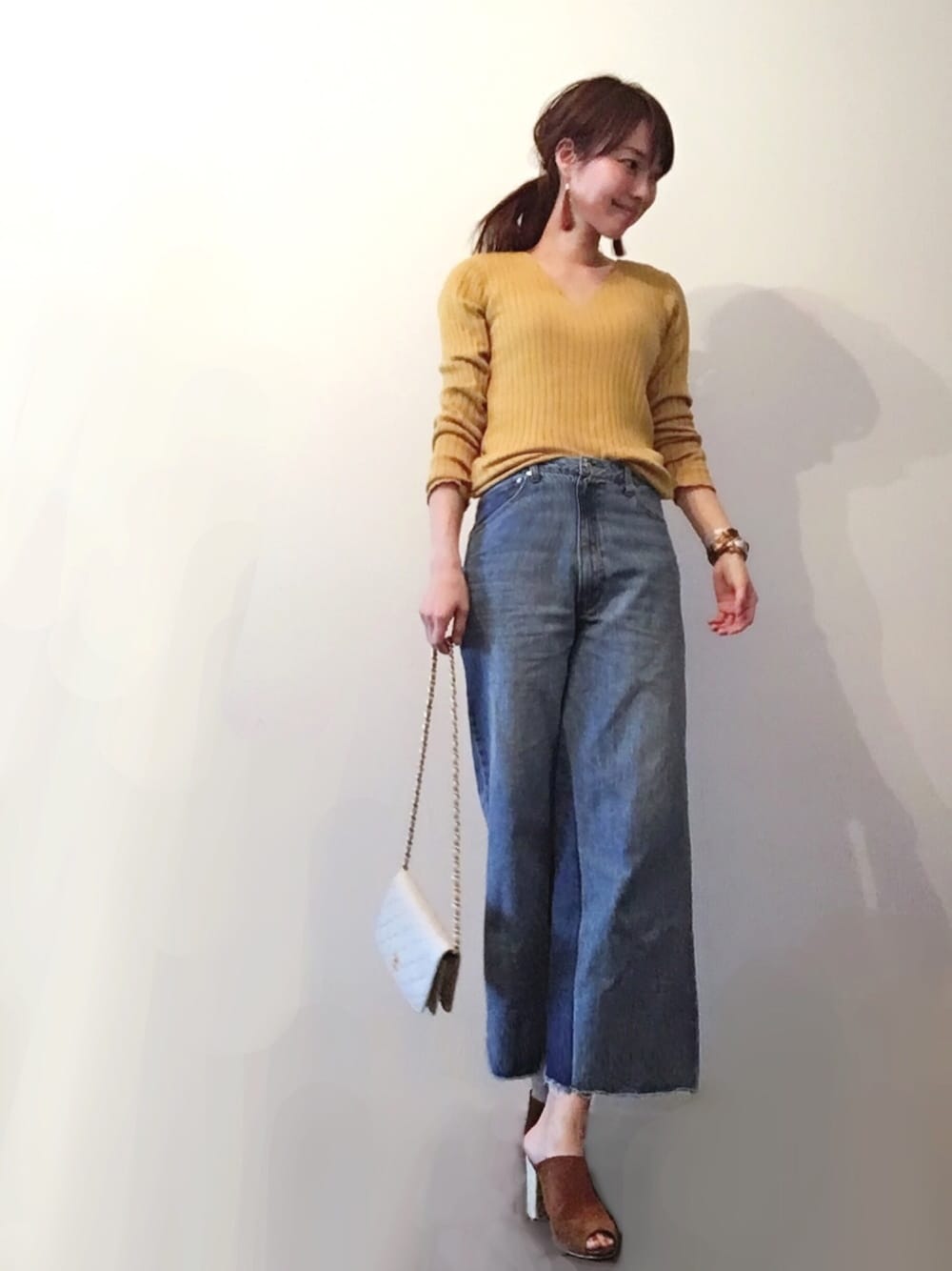 イエロー系のニット/セーター、ブルー系のデニムパンツ、ホワイト系のハンドバッグを着用したレディースの春コーディネートの1枚目の写真