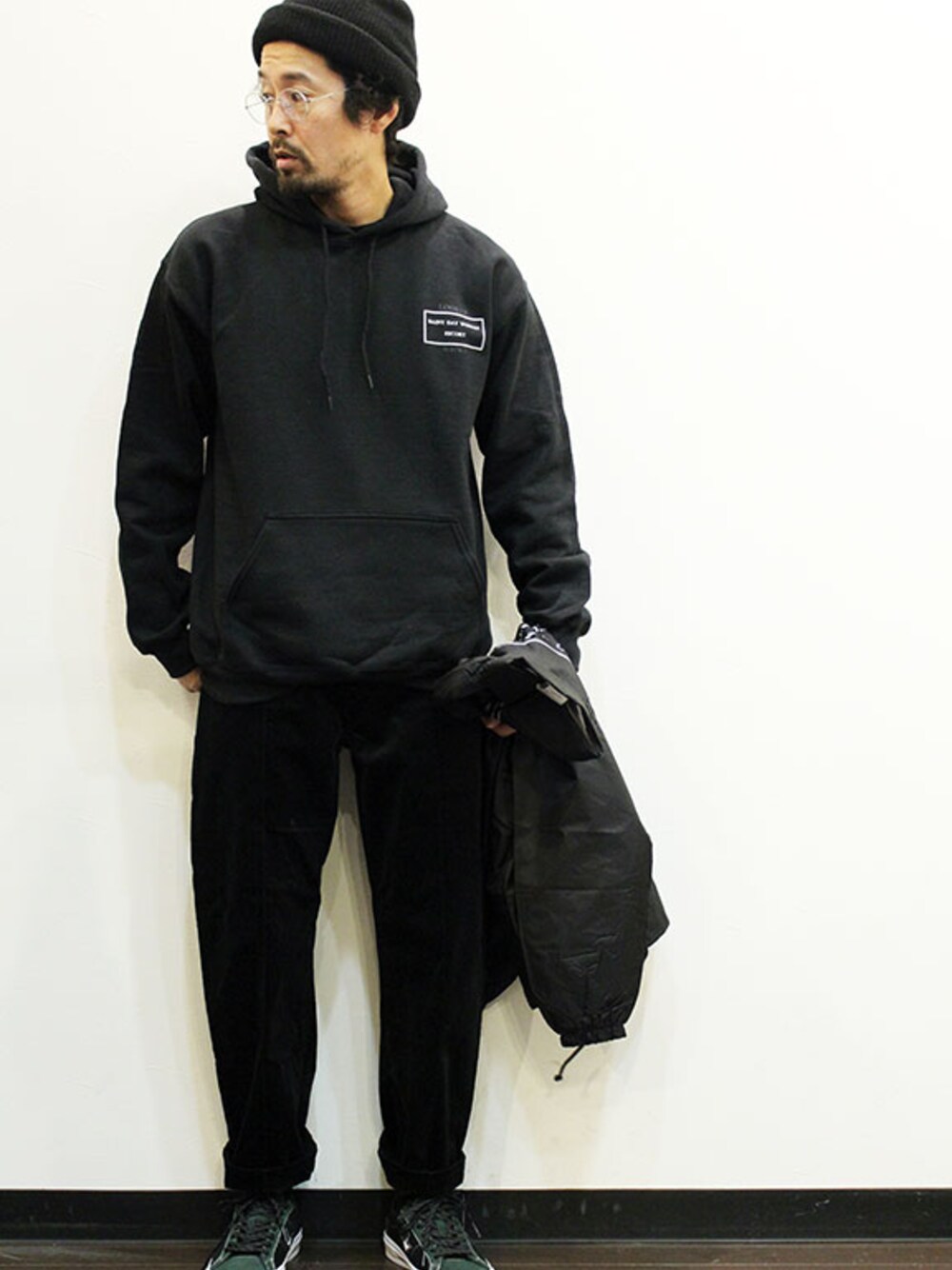 ブラック系のパーカー、グリーン系のスニーカー、ブラック系のナイロンジャケットを着用したメンズの冬コーディネートの1枚目の写真