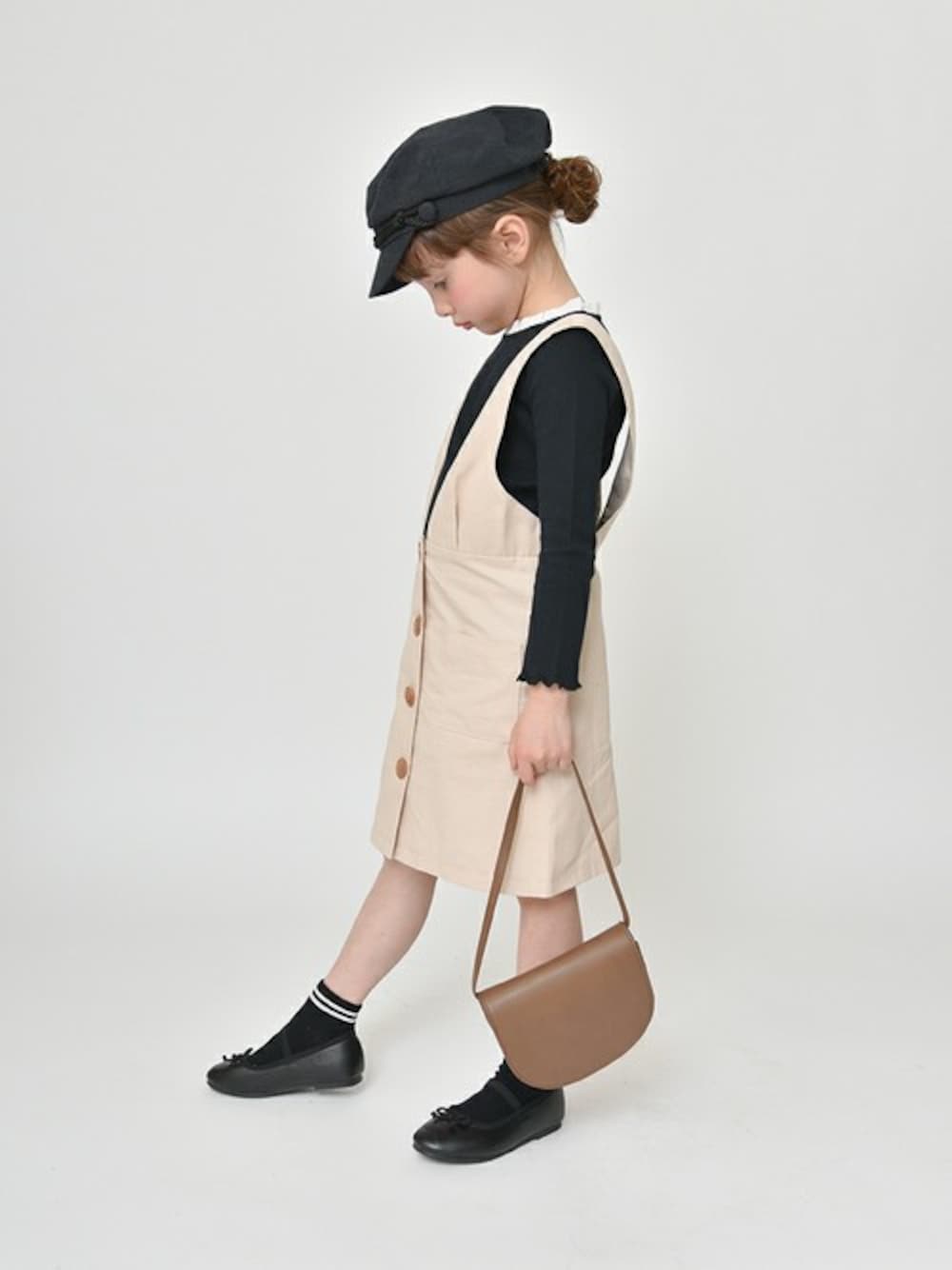 ブラック系のTシャツ/カットソー、ベージュ系のジャンパースカート、ブラウン系のショルダーバッグを着用したキッズの春コーディネートの1枚目の写真