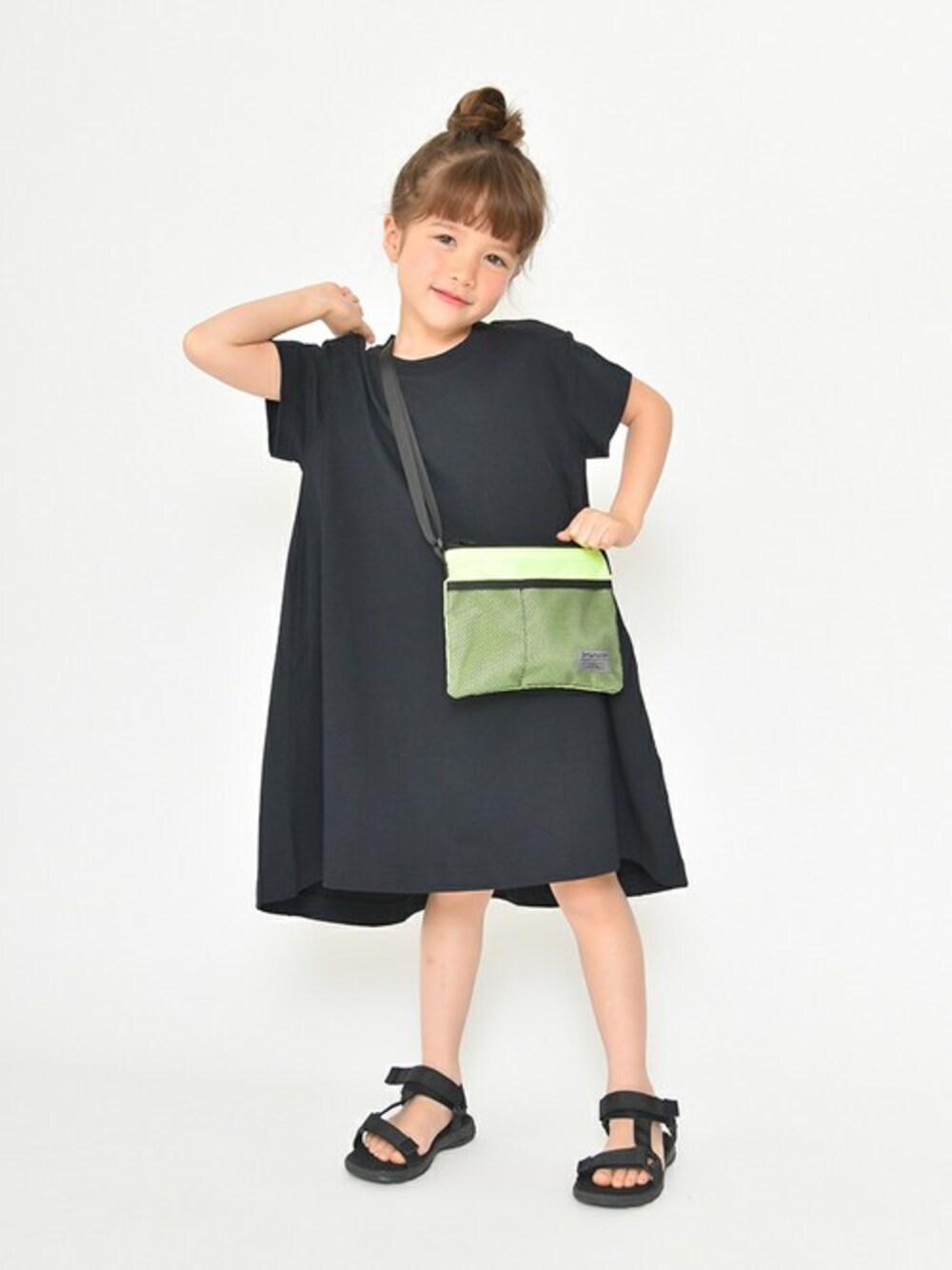 ブラック系のワンピース、グリーン系のショルダーバッグ、ブラック系のサンダルを着用したキッズの春コーディネートの1枚目の写真