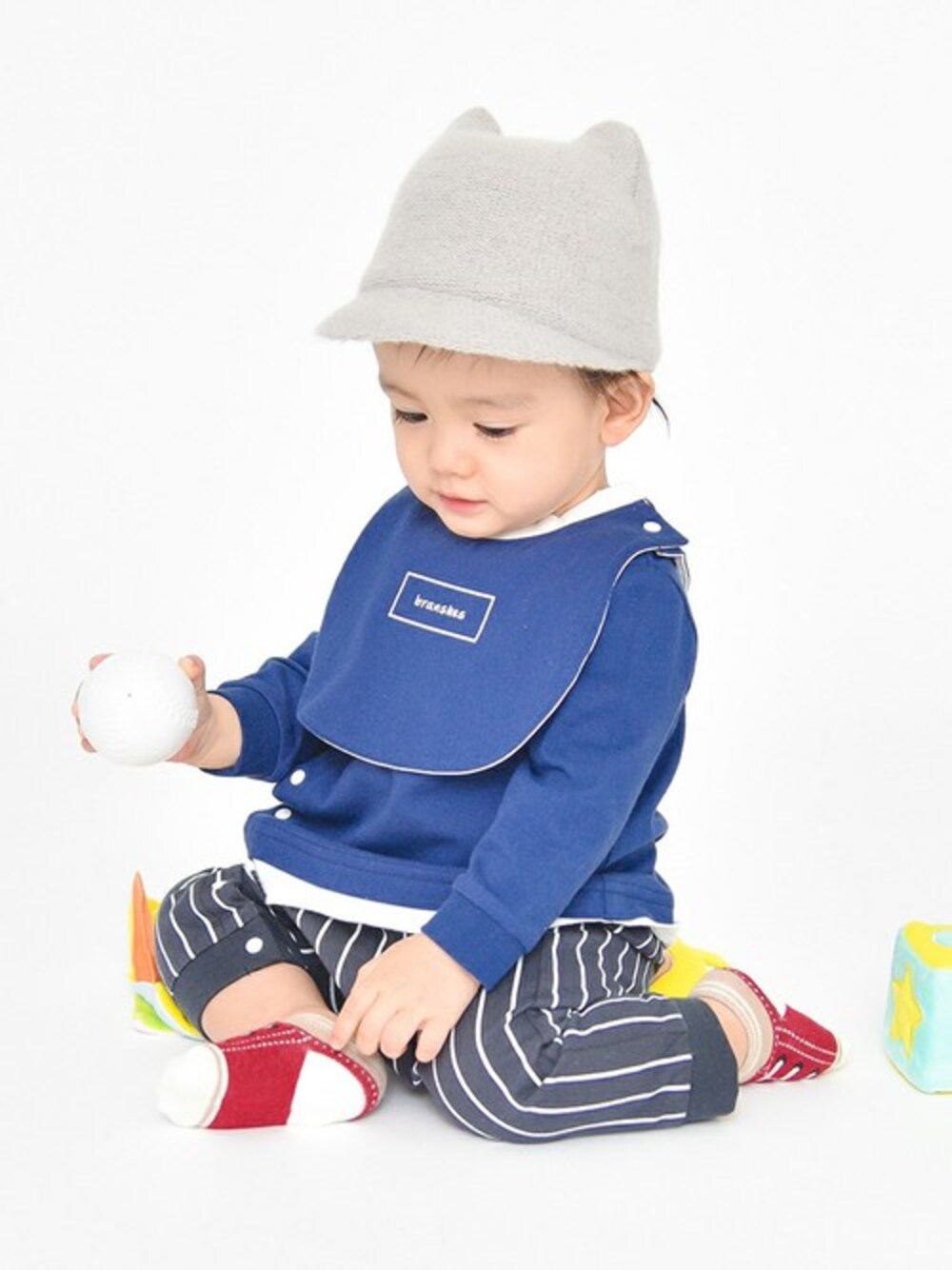 グレー系のハット、ブルー系のロンパース、ブルー系のスタイ/よだれかけを着用したキッズの夏コーディネートの1枚目の写真