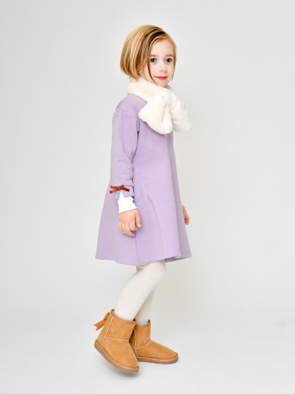 パープル系のワンピース、イエロー系のブーツ、ホワイト系のマフラーを着用したキッズの冬コーディネートの1枚目の写真