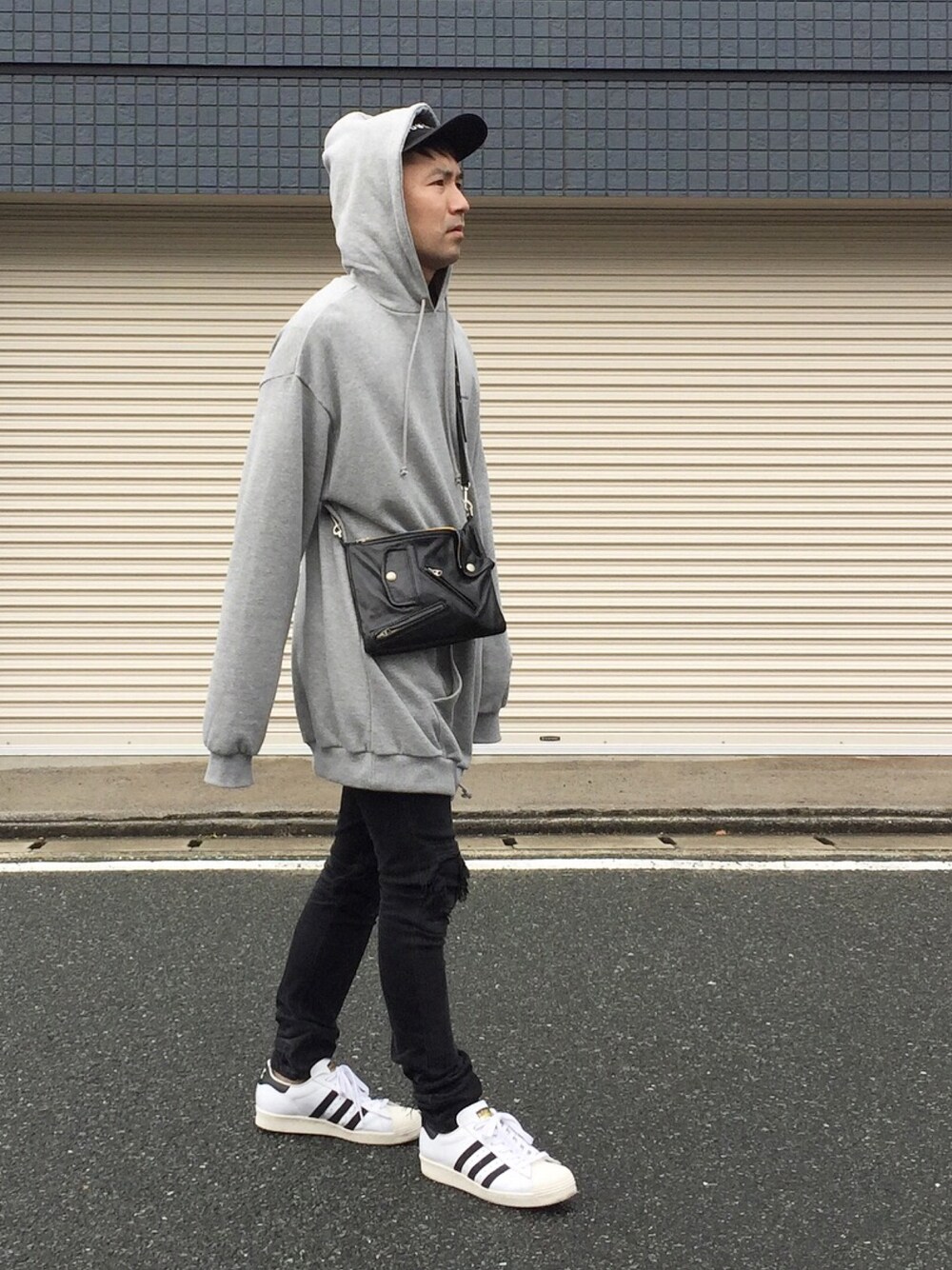 グレー系のパーカー、ブラック系のデニムパンツ、ブラック系のバッグを着用したメンズの春コーディネートの1枚目の写真