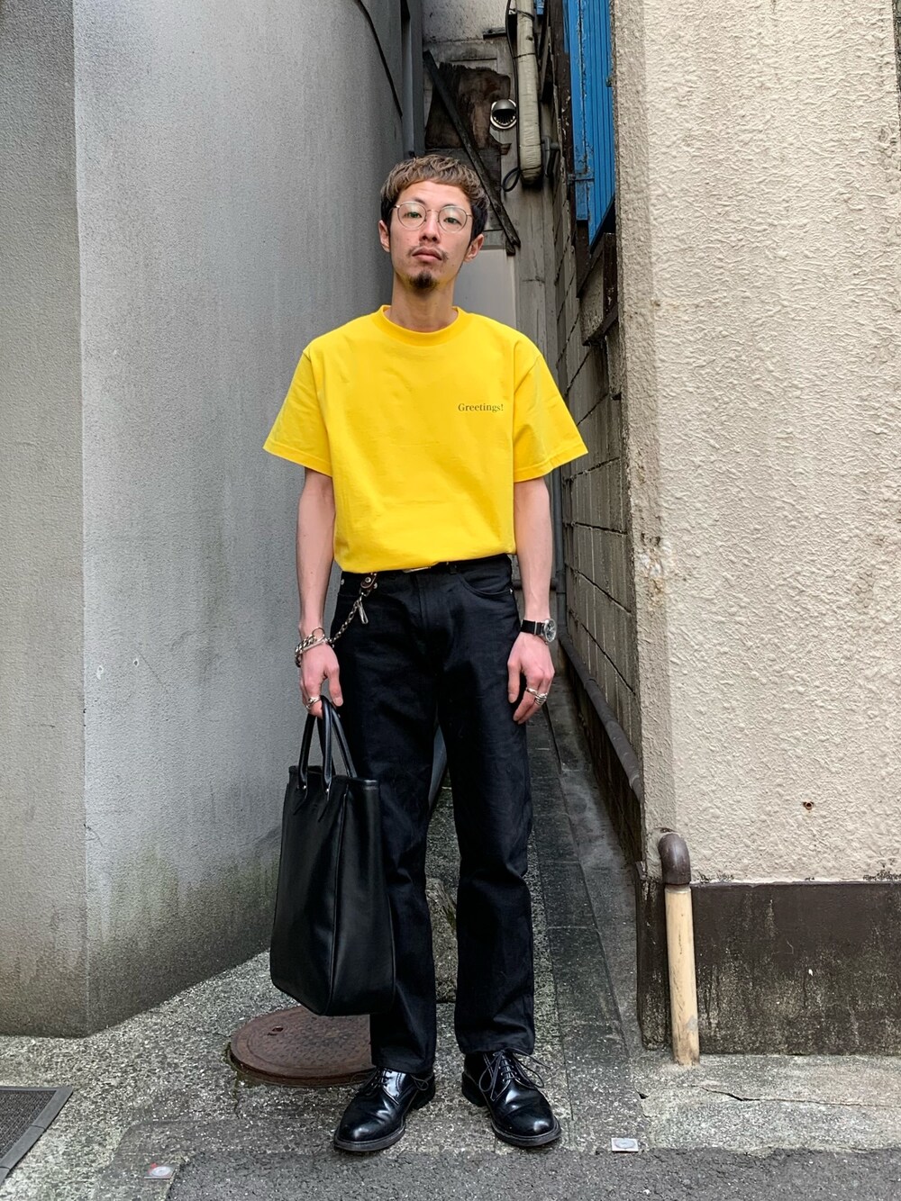 イエロー系のTシャツ/カットソー、ブラック系のデニムパンツ、ブラック系のトートバッグを着用したメンズの春コーディネートの1枚目の写真