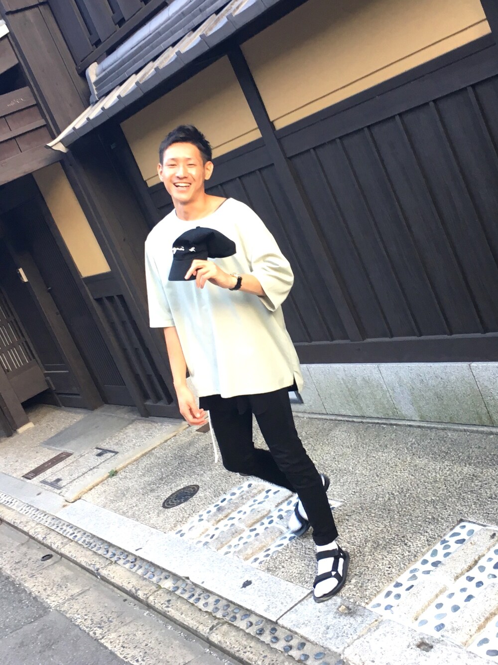 ベージュ系のTシャツ/カットソー、ブラック系のサンダル、ブラック系のキャップを着用したメンズの夏コーディネートの1枚目の写真