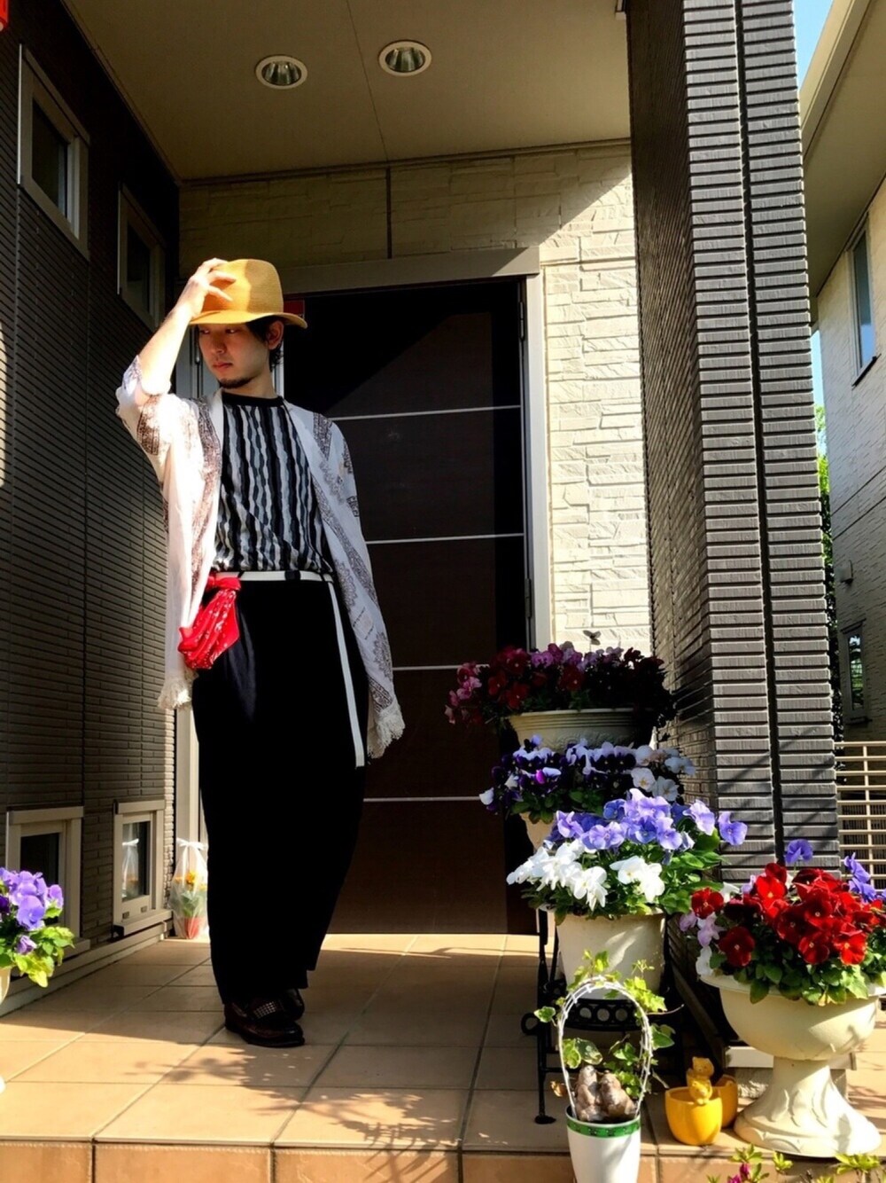 グレー系のトップス、ホワイト系のカーディガン/ボレロ、レッド系のパンツを着用したメンズの春コーディネートの1枚目の写真