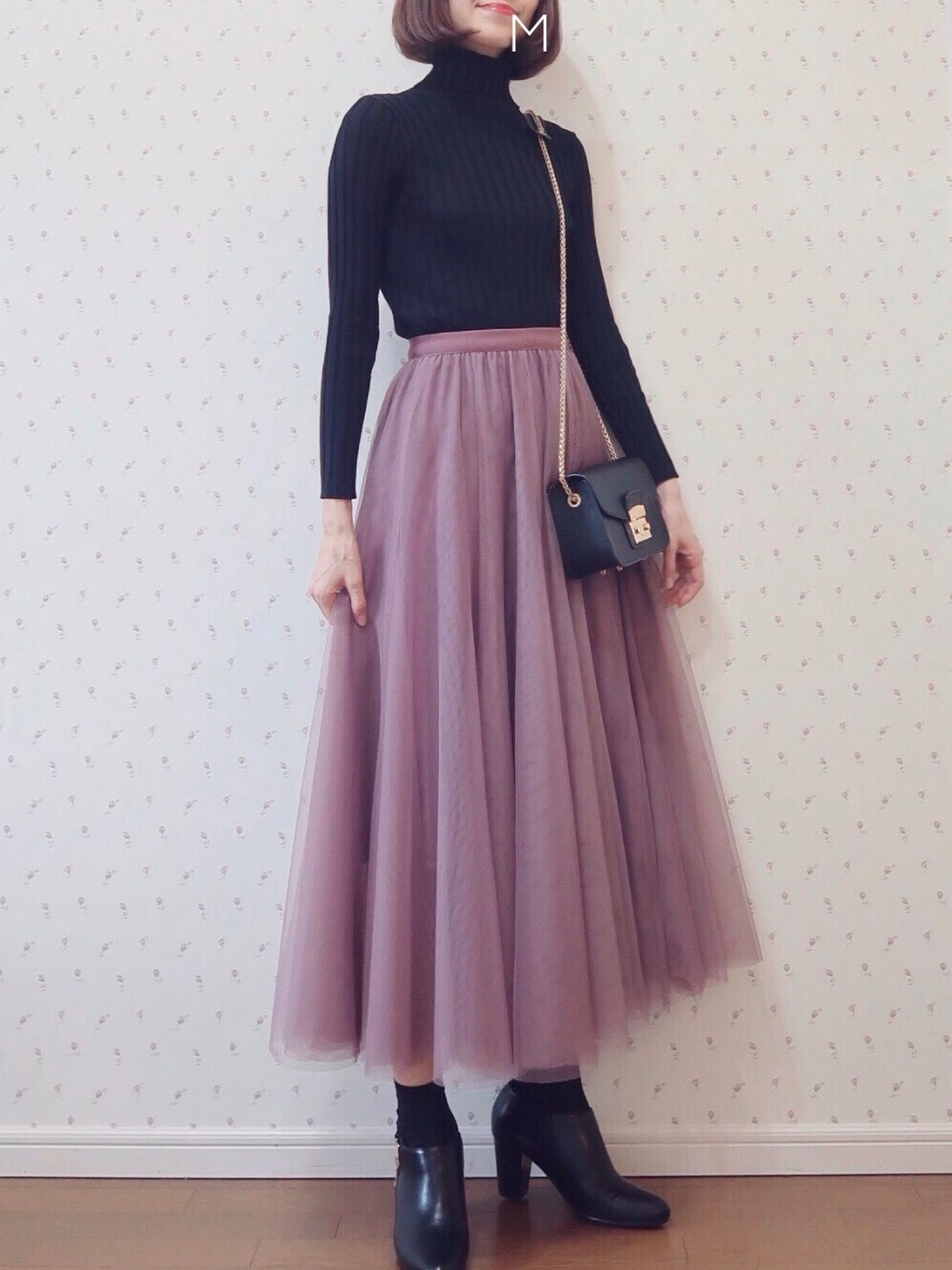 ピンク系のスカート、ブラック系のニット/セーター、ブラック系のショルダーバッグを着用したレディースの秋コーディネートの1枚目の写真
