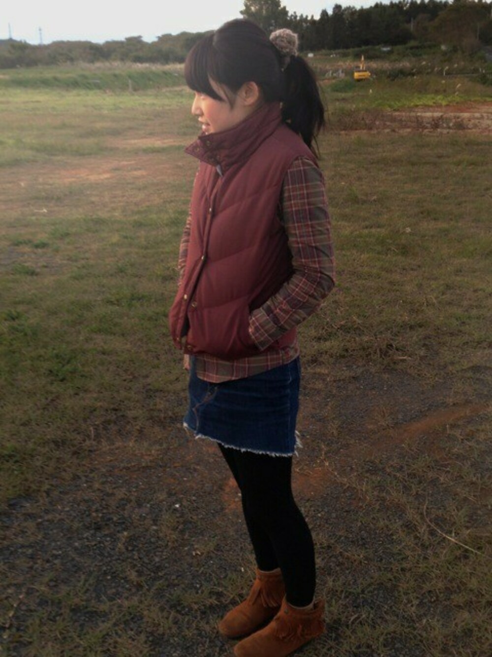 ブルー系のデニムスカート、レッド系のダウンベスト、ブラウン系のブーツを着用したレディースの秋コーディネートの1枚目の写真