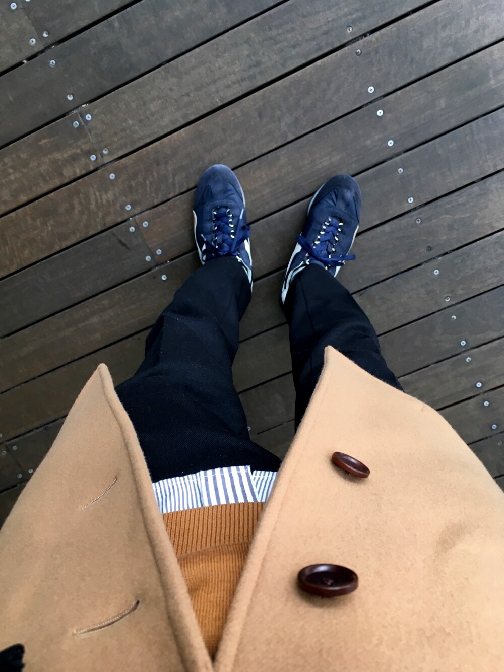 ブルー系のスニーカー、ブラック系のスラックス、ベージュ系のチェスターコートを着用したメンズの冬コーディネートの1枚目の写真