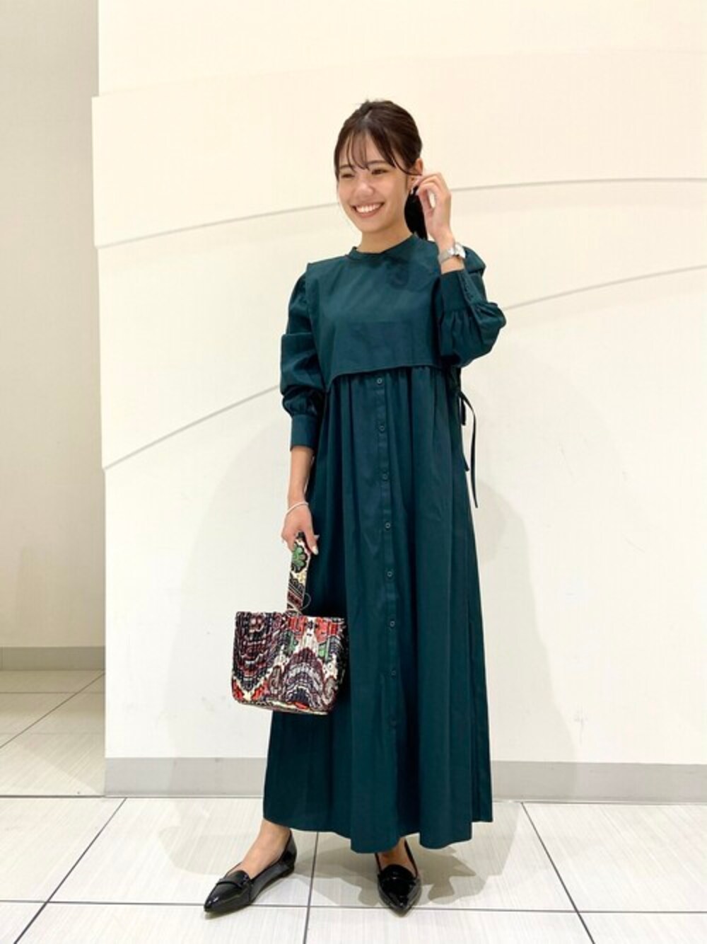 グリーン系のワンピース、ブラック系のパンプス、レッド系のショルダーバッグを着用したレディースの秋コーディネートの1枚目の写真