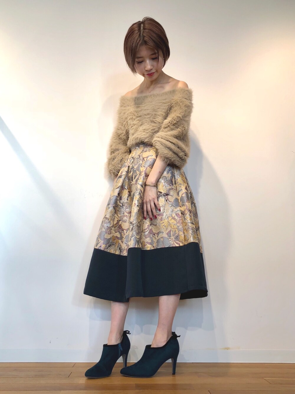 ベージュ系のスカート、グリーン系のブーティを着用したレディースの冬コーディネートの1枚目の写真