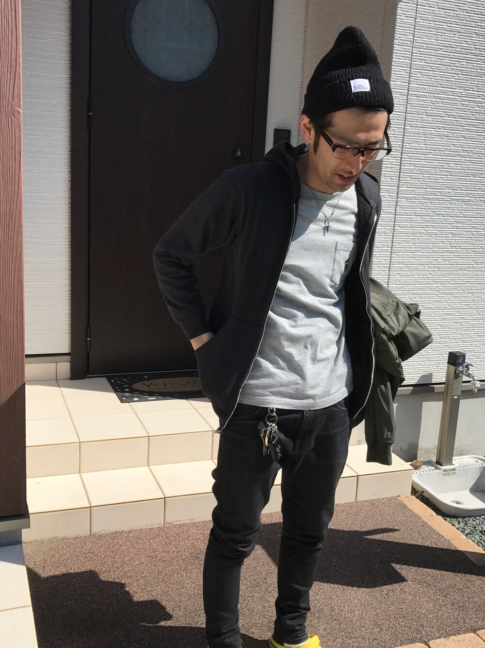 「春コーデ、カーキ、スキニー、ニット帽、めがね、黒コーデ、黒スキニー」｜「RAGEBLUEの【BRONER/ブローナー】ワッチ/542041（ニットキャップ/ビーニー、ブラック系）」を使った、ハナさん（メンズ・174cm）の春コーディネートの1枚目の写真