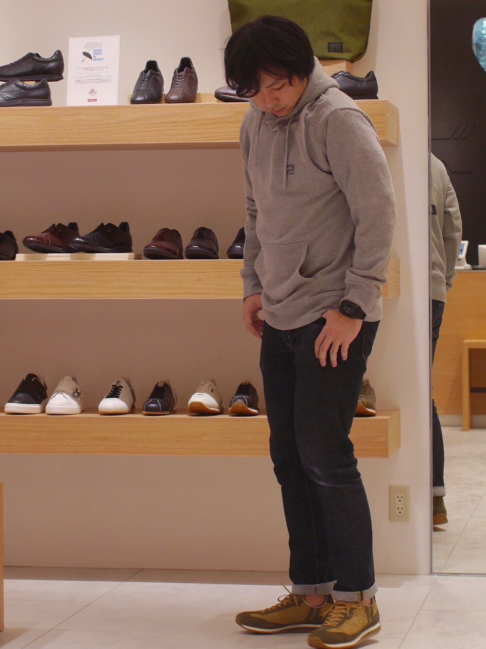 グレー系のパーカー、ブルー系のデニムパンツ、グリーン系のスニーカーを着用したメンズの冬コーディネートの1枚目の写真