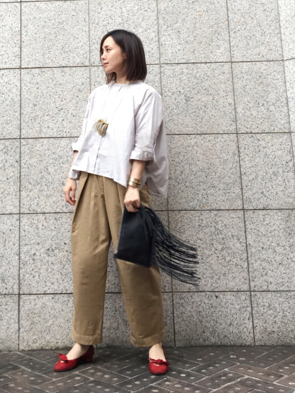 レッド系のパンプス、ベージュ系のチノパンツ、ブラック系のクラッチバッグを着用したレディースの秋コーディネートの1枚目の写真