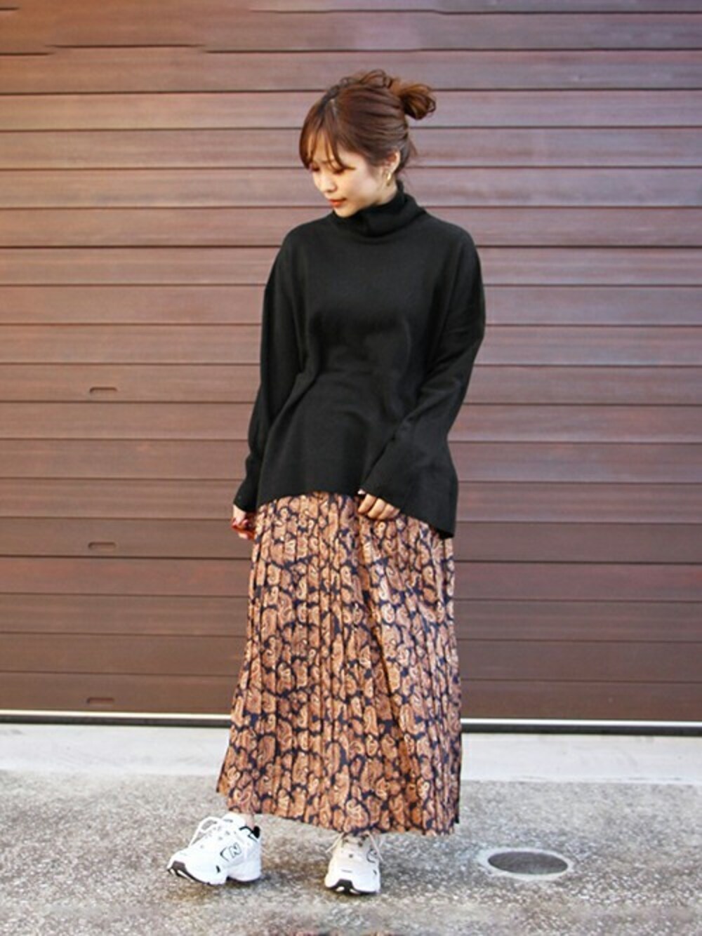 ブラック系のニット/セーター、ブラウン系のスカート、ホワイト系のスニーカーを着用したレディースの秋コーディネートの1枚目の写真