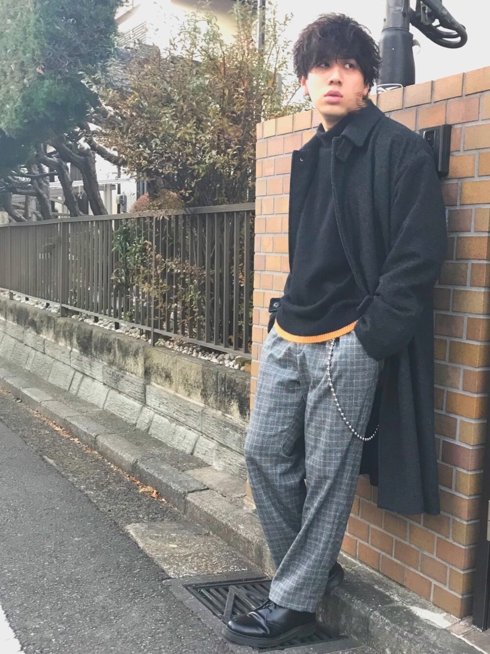 グレー系のステンカラーコート、ブラック系のニット/セーター、グレー系のスラックスを着用したメンズの冬コーディネートの1枚目の写真