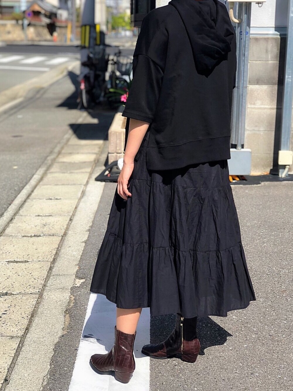 ブラック系のパーカー、ブラック系のスカート、ブラウン系のブーツを着用したレディースの秋コーディネートの1枚目の写真