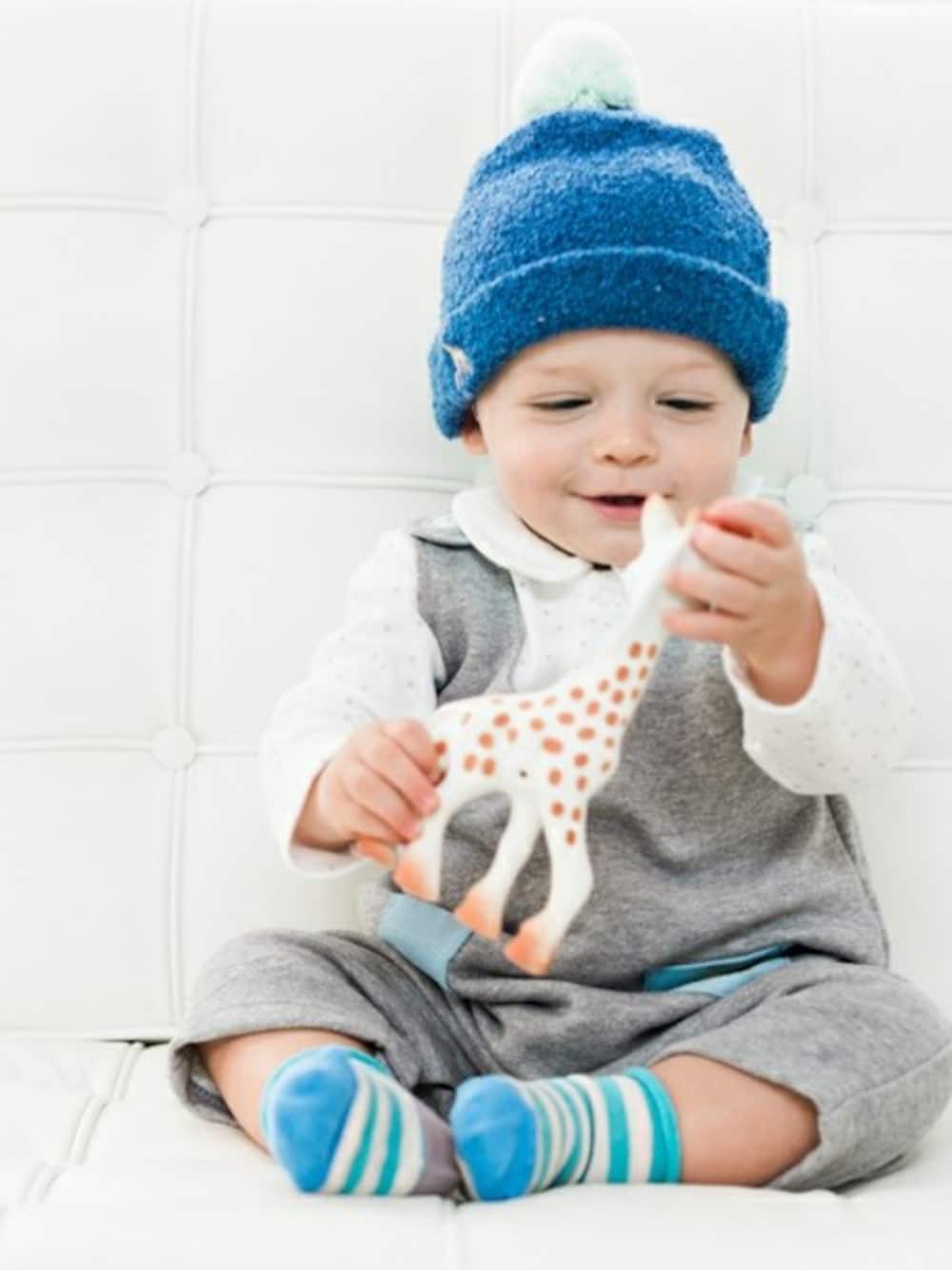 グレー系のサロペット/オーバーオール、ホワイト系のロンパース、ブルー系のキャップを着用したキッズの冬コーディネートの1枚目の写真