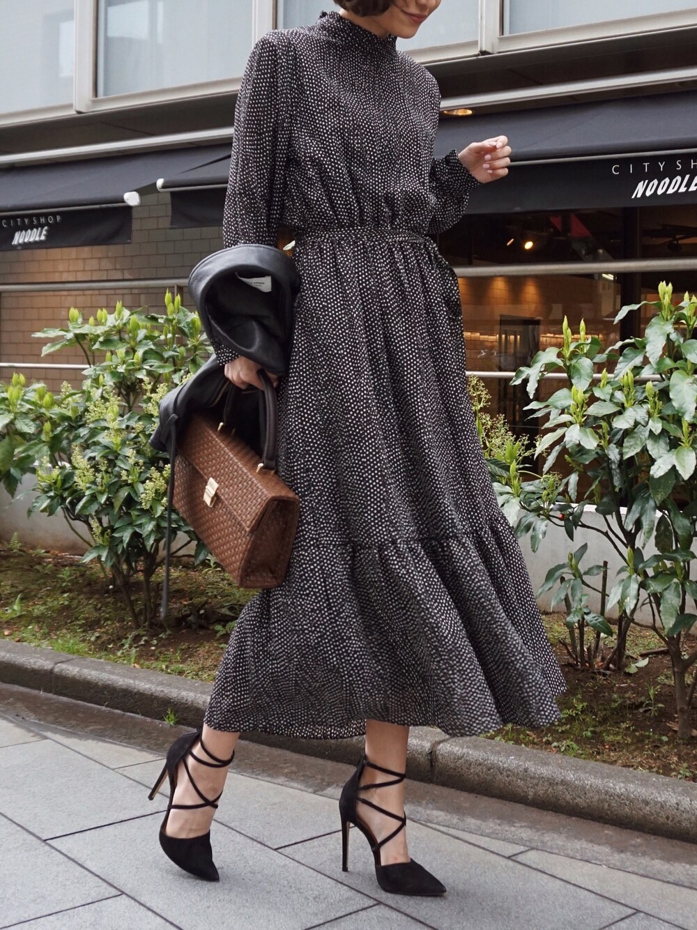 ブラック系のワンピース、ブラウン系のハンドバッグを着用したレディースの春コーディネートの1枚目の写真