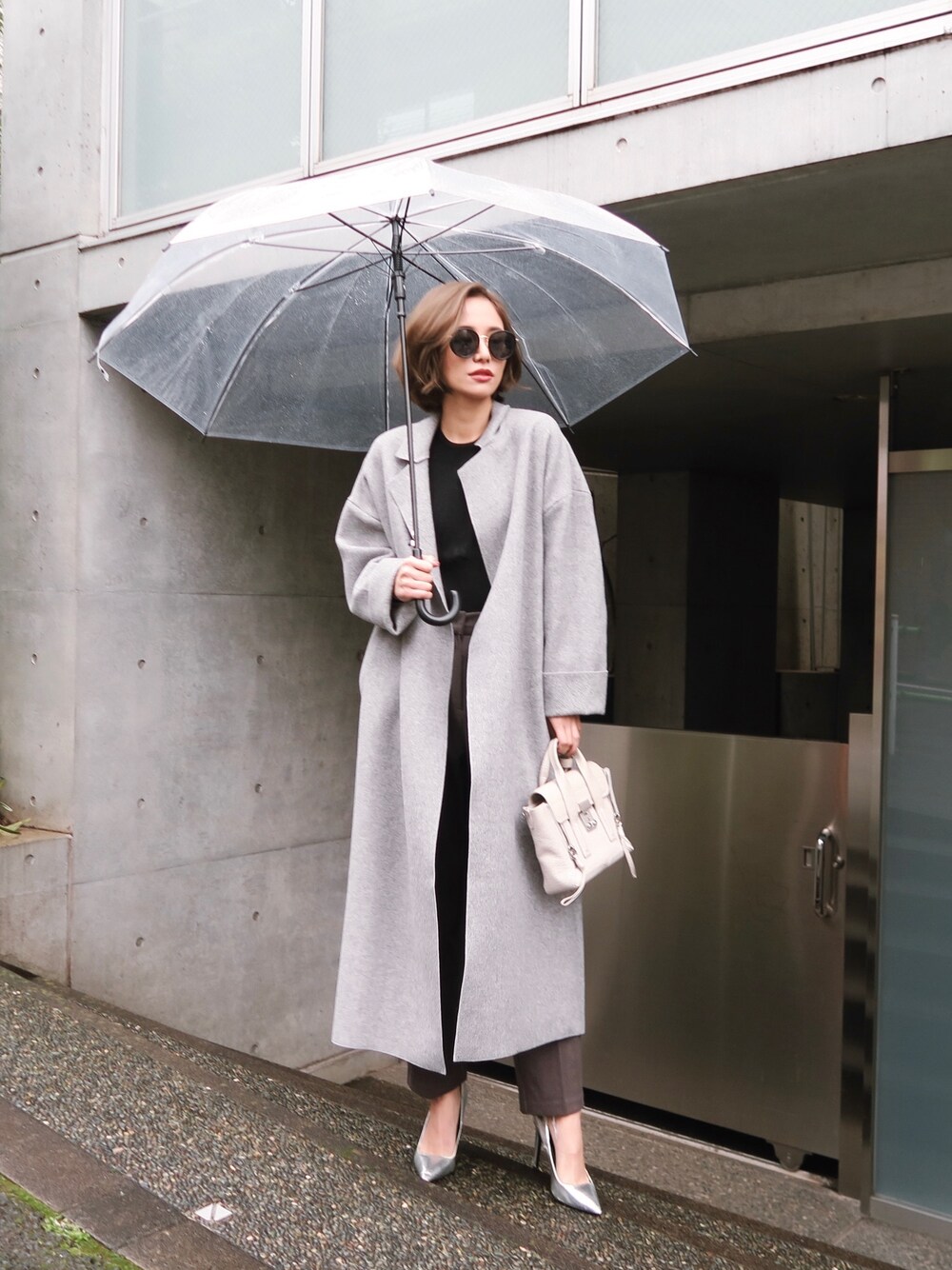 グレー系のチェスターコート、グレー系のスラックスを着用したレディースの冬コーディネートの1枚目の写真