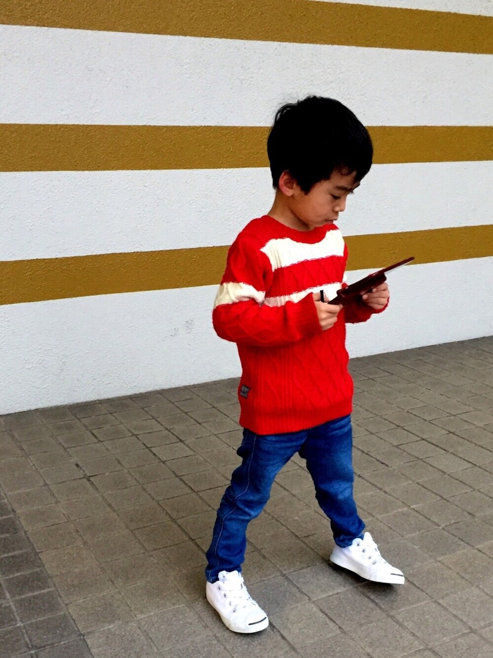 レッド系のニット/セーター、ブルー系のデニムパンツ、ホワイト系のスニーカーを着用したキッズの冬コーディネートの1枚目の写真