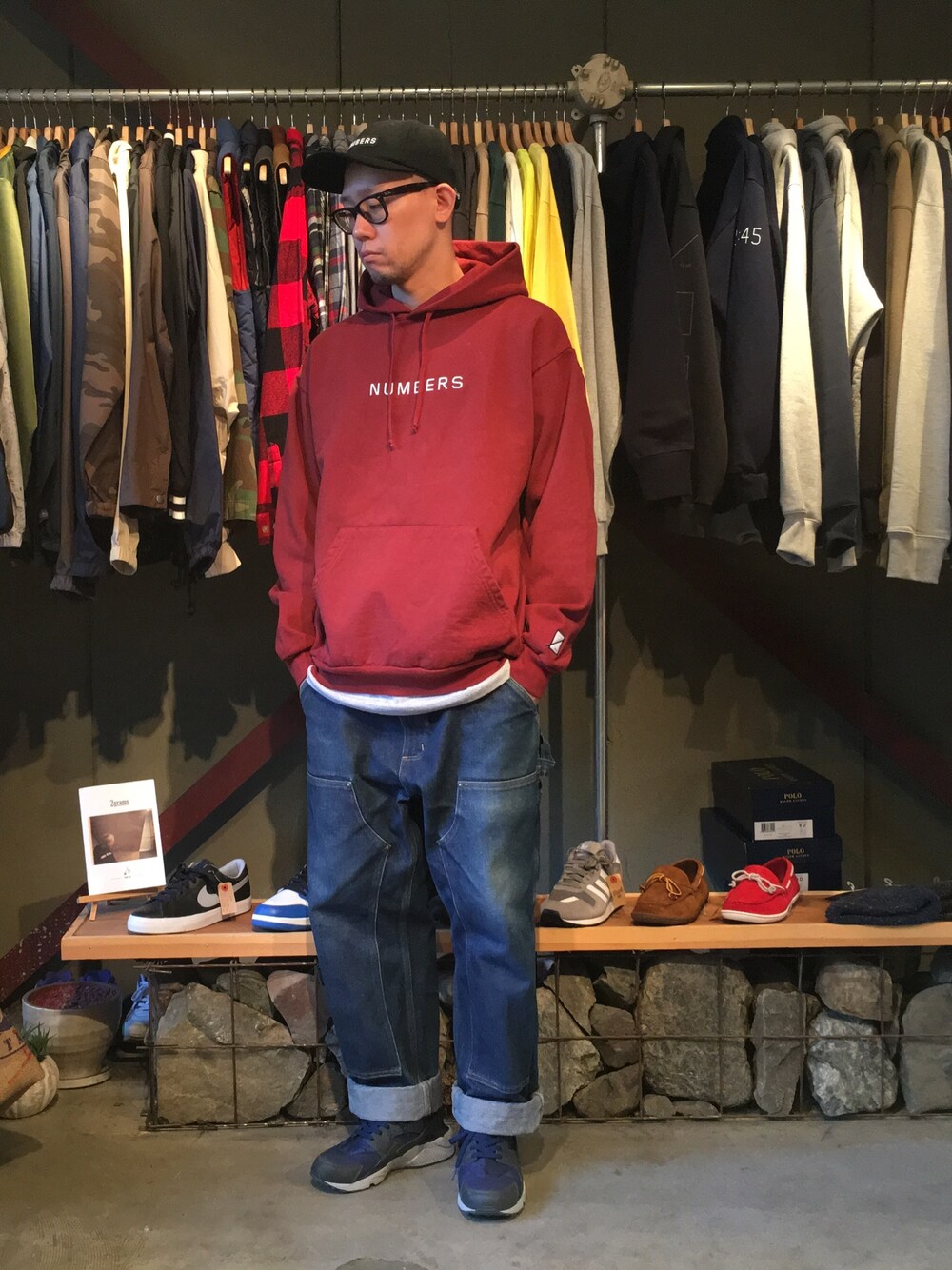 レッド系のパーカー、ブルー系のデニムパンツ、ブルー系のスニーカーを着用したメンズの秋コーディネートの1枚目の写真