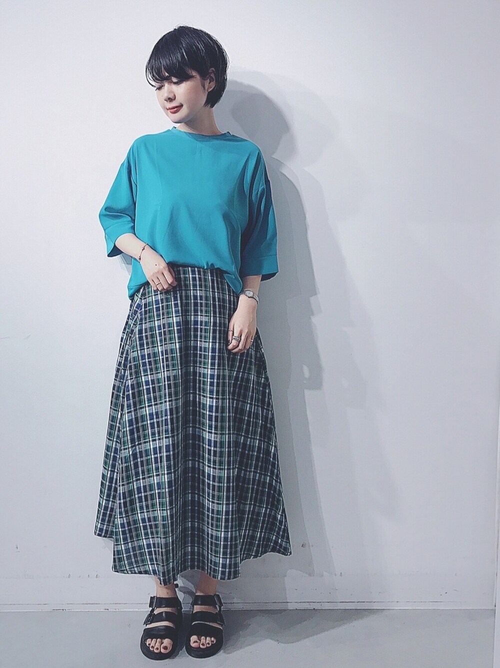 グリーン系のTシャツ/カットソー、グリーン系のスカート、ブラック系のサンダルを着用したレディースの春コーディネートの1枚目の写真