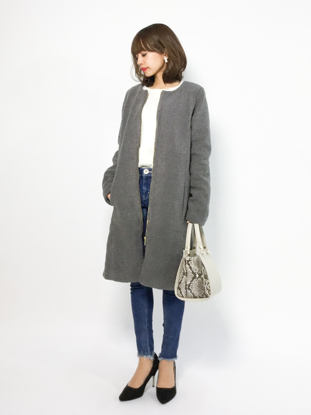 グレー系のノーカラージャケット、ホワイト系のニット/セーター、ブルー系のデニムパンツを着用したレディースの冬コーディネートの1枚目の写真