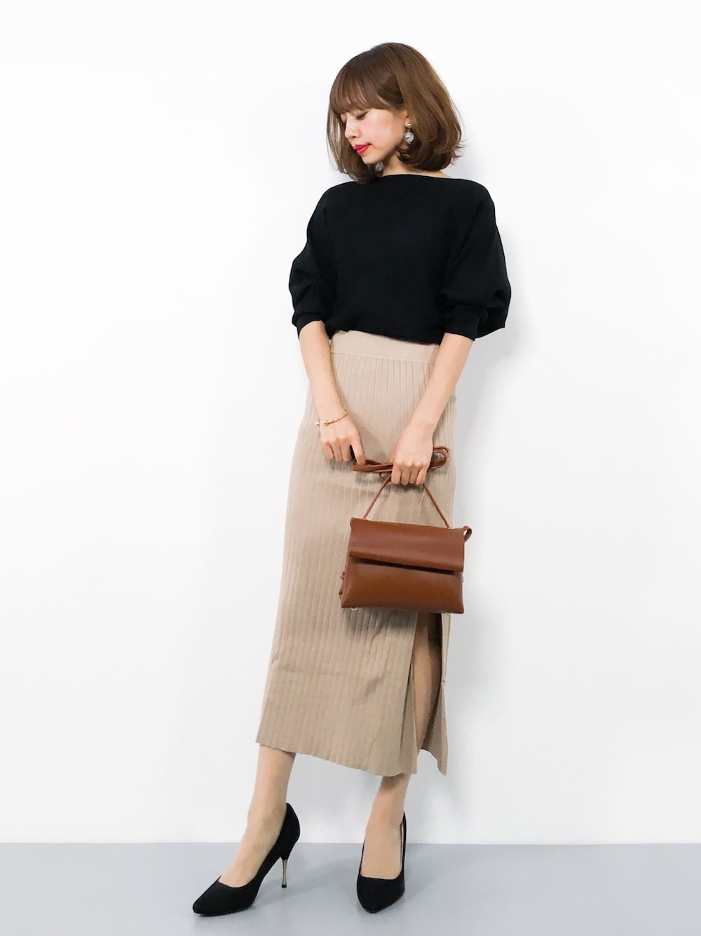 ブラック系のニット/セーター、ベージュ系のスカート、イエロー系のショルダーバッグを着用したレディースの秋コーディネートの1枚目の写真