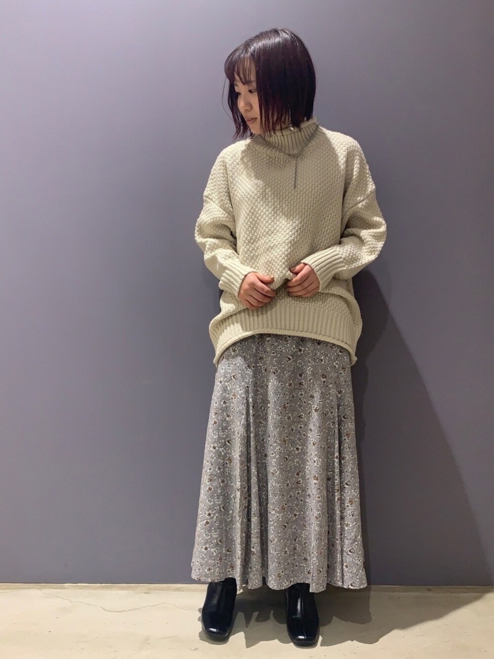 ホワイト系のニット/セーター、グレー系のスカート、ブラウン系のブーツを着用したレディースの冬コーディネートの1枚目の写真