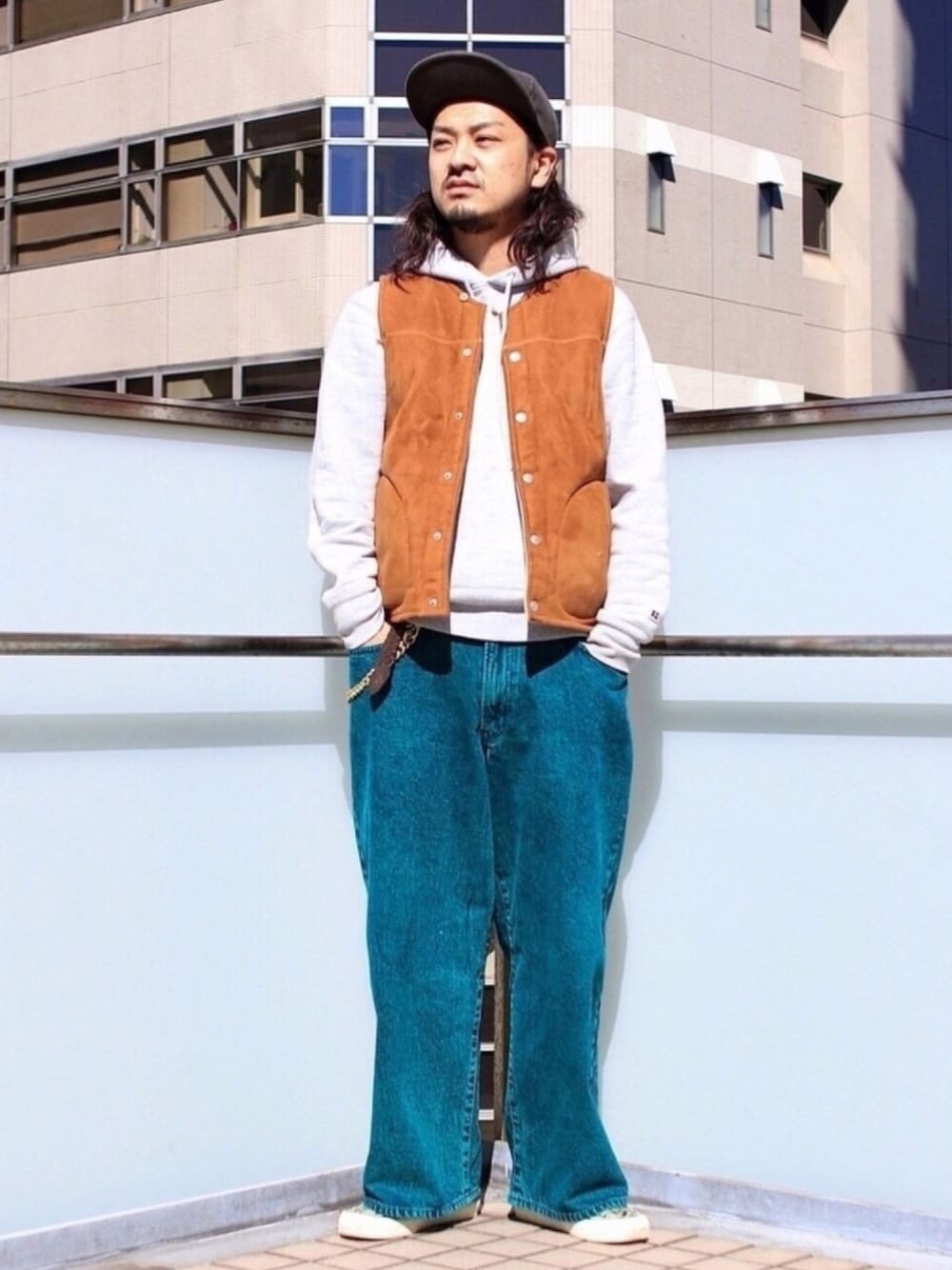 ブラウン系のベスト、グレー系のパーカー、グリーン系のデニムパンツを着用したメンズの秋コーディネートの1枚目の写真