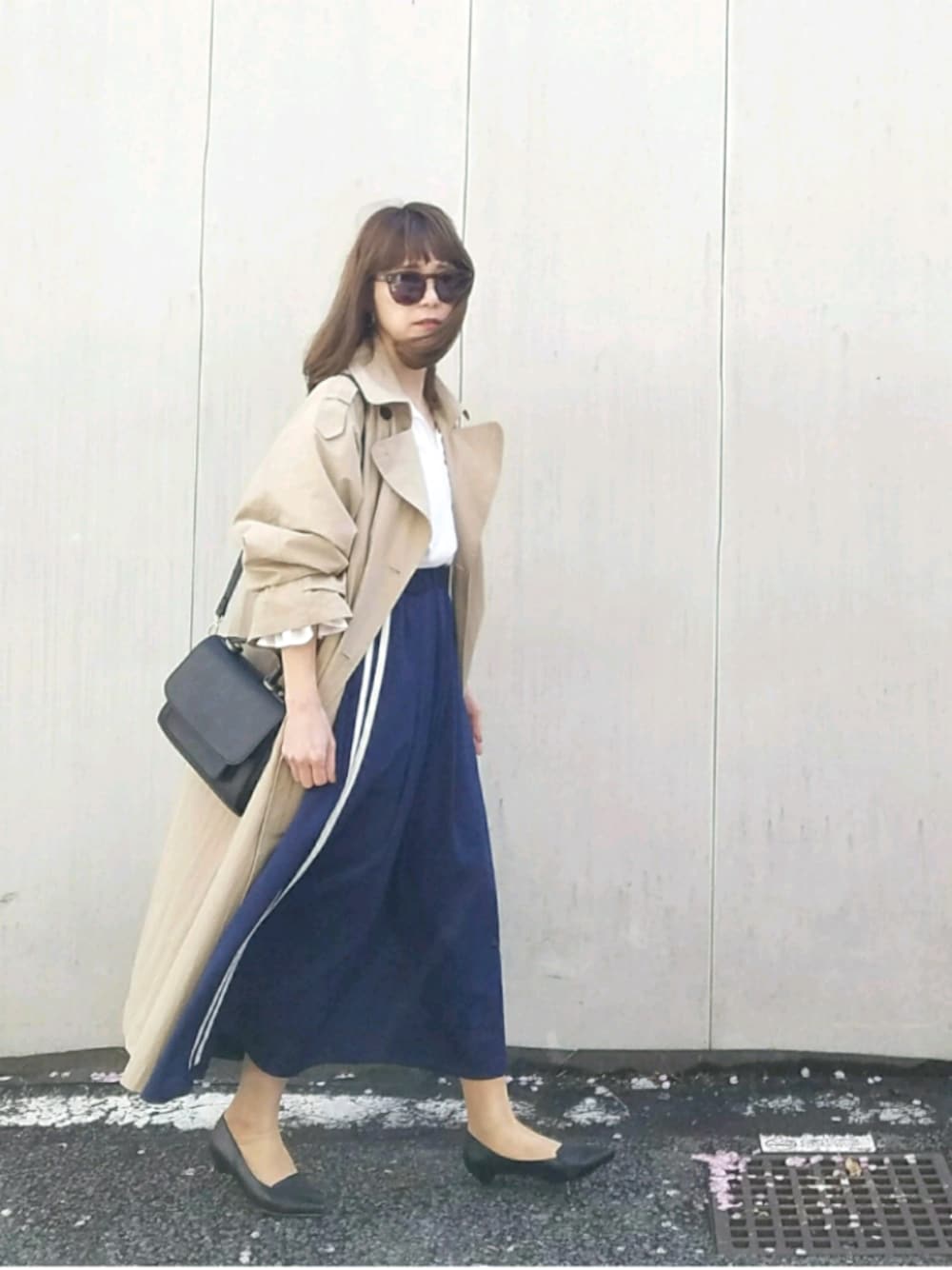 ベージュ系のトレンチコート、ブルー系のスカート、その他のピアス（両耳用）を着用したレディースの春コーディネートの1枚目の写真