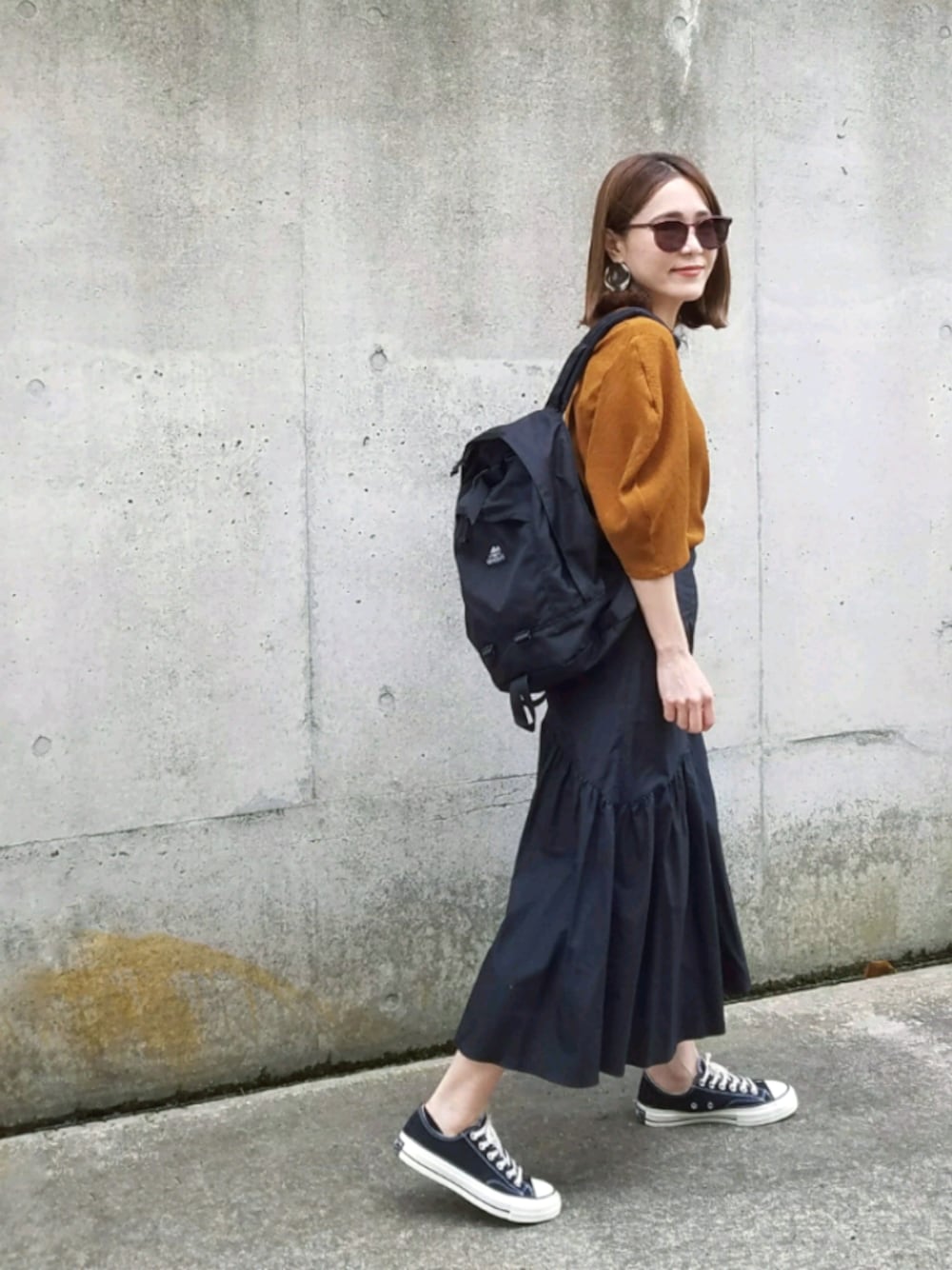 ブラック系のスカート、ブラック系のスニーカー、ブラック系のバックパック/リュックを着用したレディースの夏コーディネートの1枚目の写真