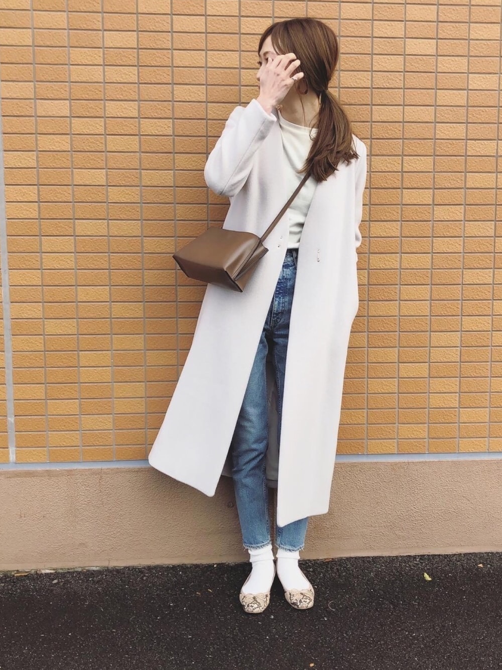 グレー系のノーカラーコート、ベージュ系のTシャツ/カットソー、ブルー系のデニムパンツを着用したレディースの冬コーディネートの1枚目の写真